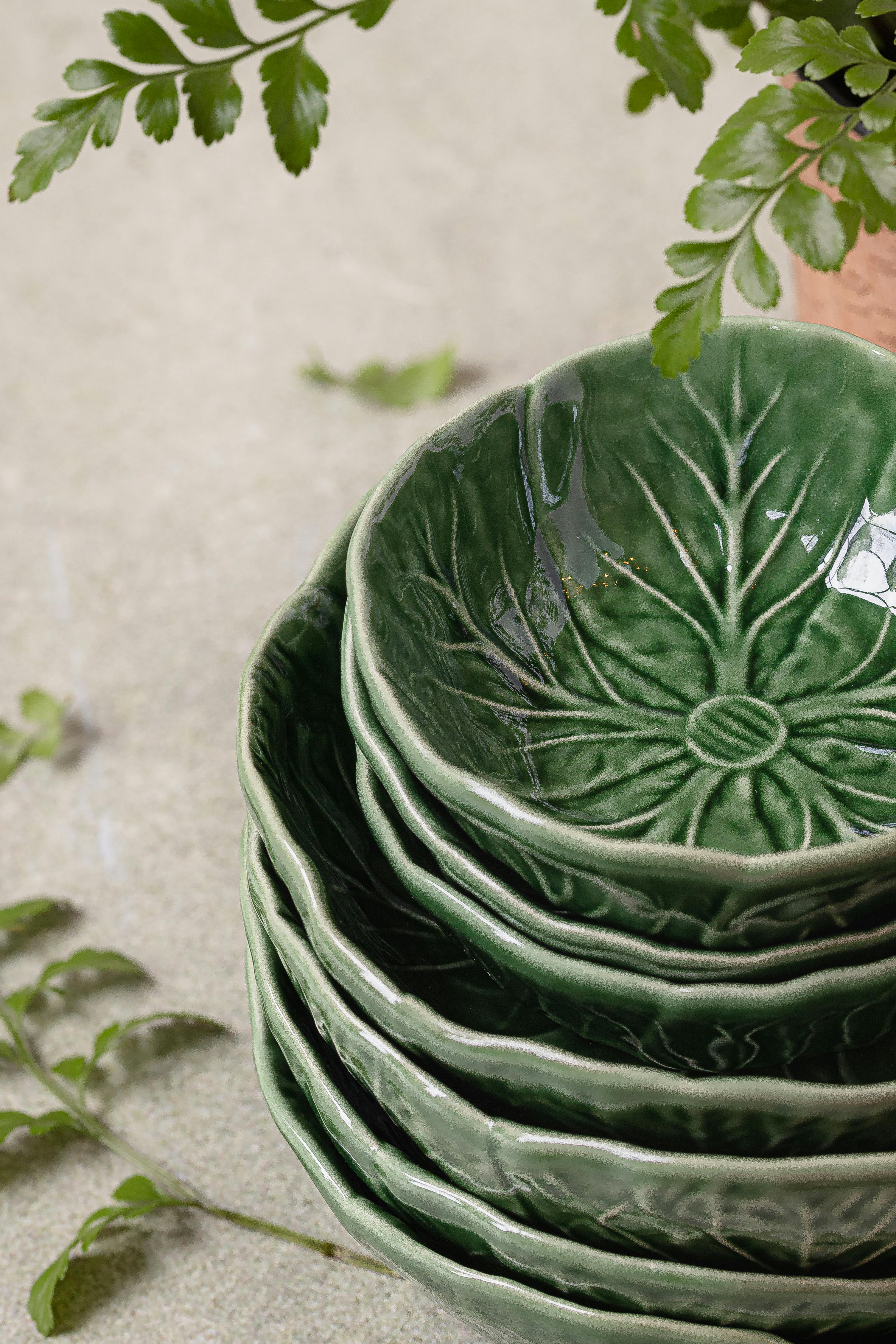 A stack of green ceramic bowls with a leaf pattern, ideal for elegant dining settings, captured in a vertical shot.