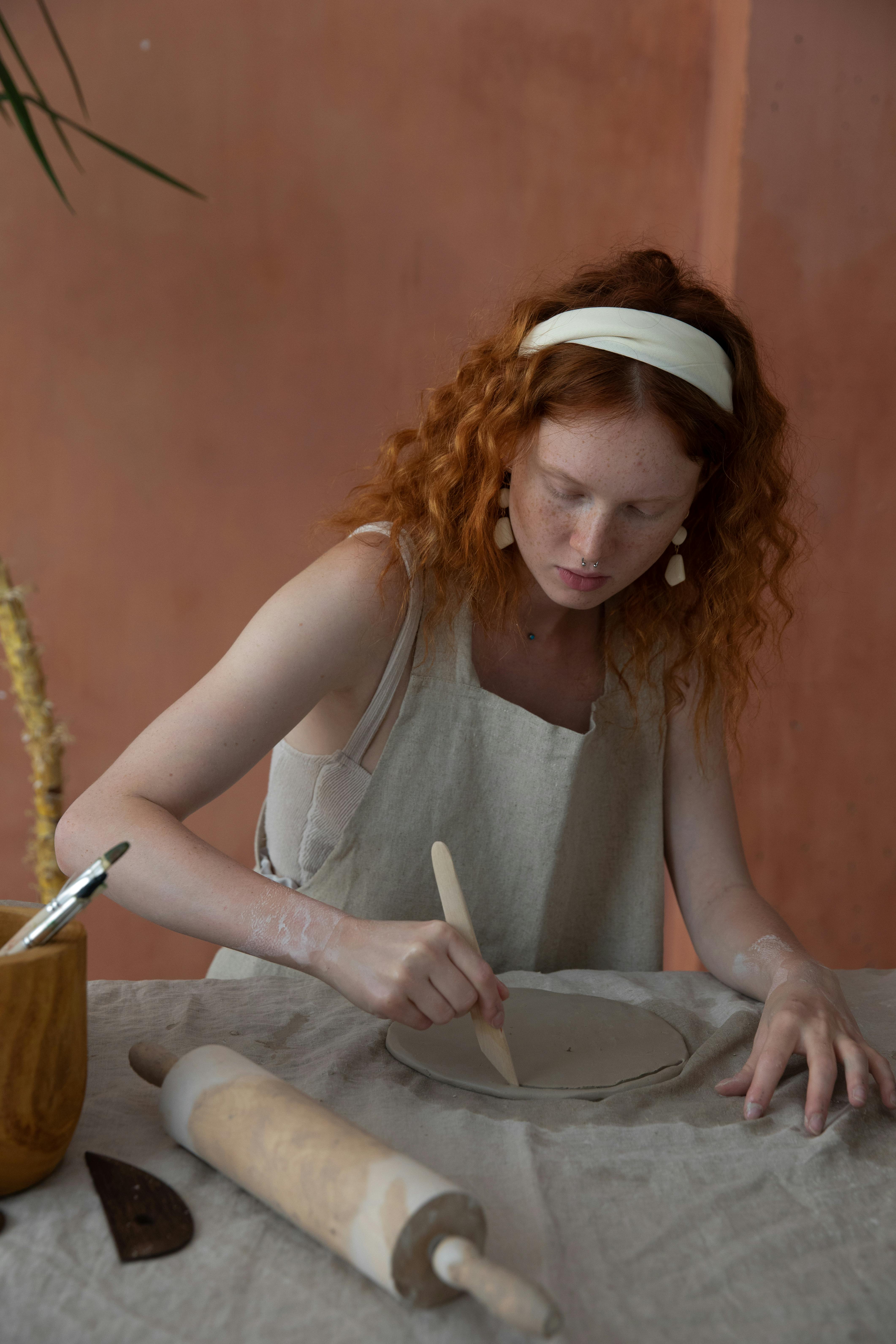 A focused woman shaping a ceramic plate by hand in a crafting workshop, showcasing artisan skills.