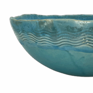 A glazed turquoise ceramic bowl with wavy surface patterns.