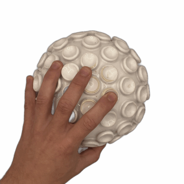 A hand touching a white spherical object with circular protrusions on its surface.