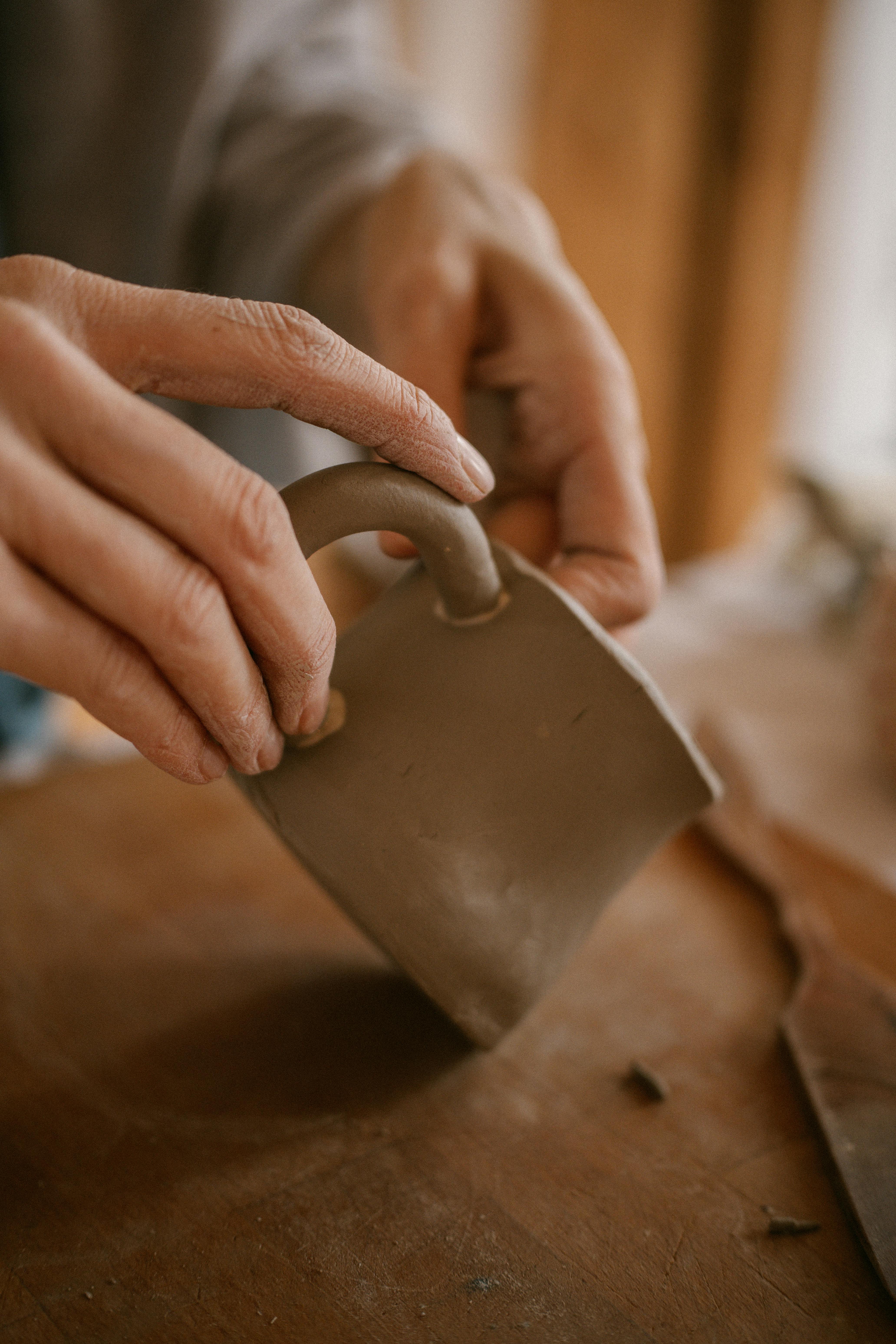 Close-up of hands shaping a clay mug, capturing artisanal craftsmanship and creativity.