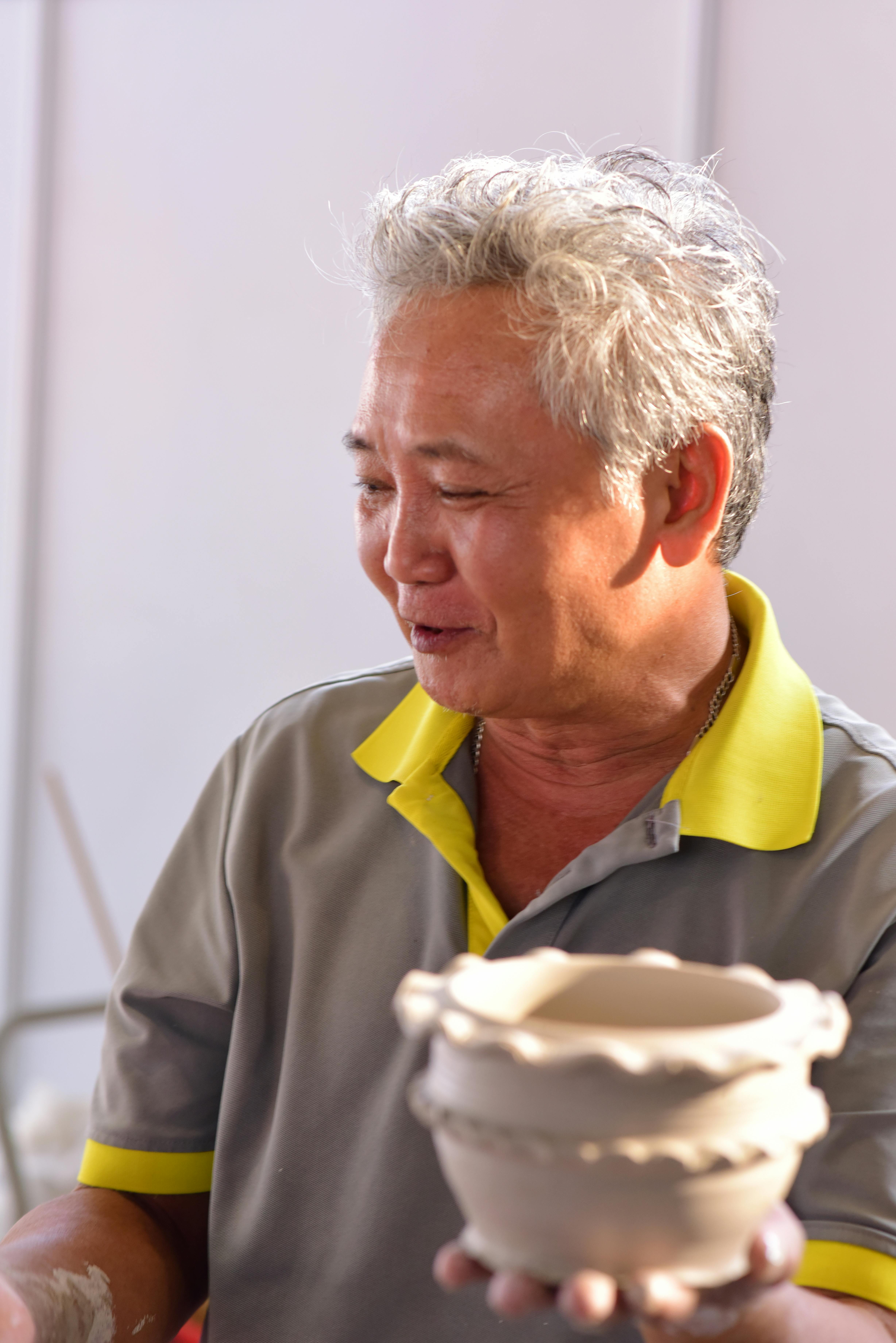 Elderly potter showcasing a handmade ceramic bowl, highlighting traditional pottery skills.