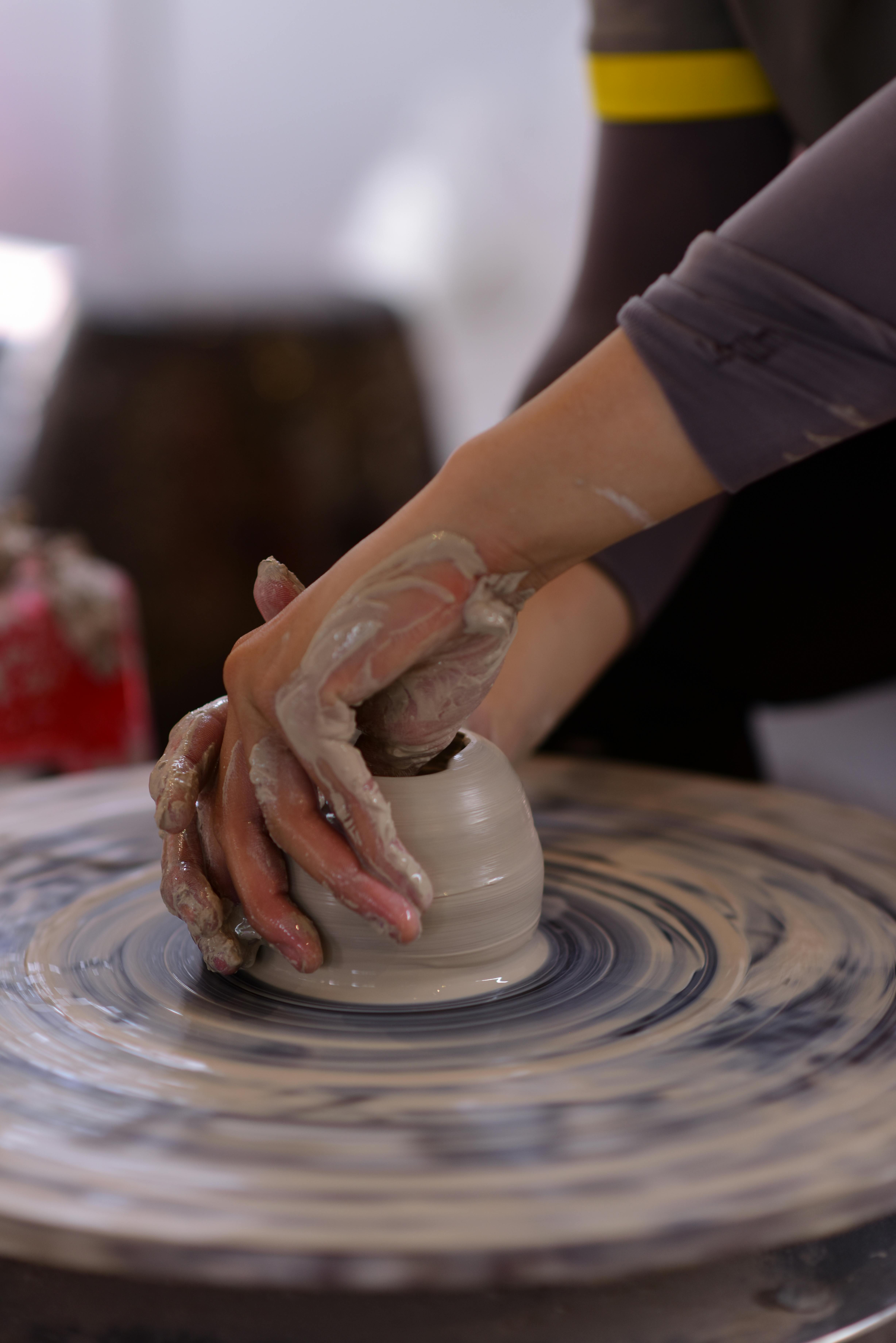 Hands crafting a clay pot on a pottery wheel, showcasing traditional handmade techniques.