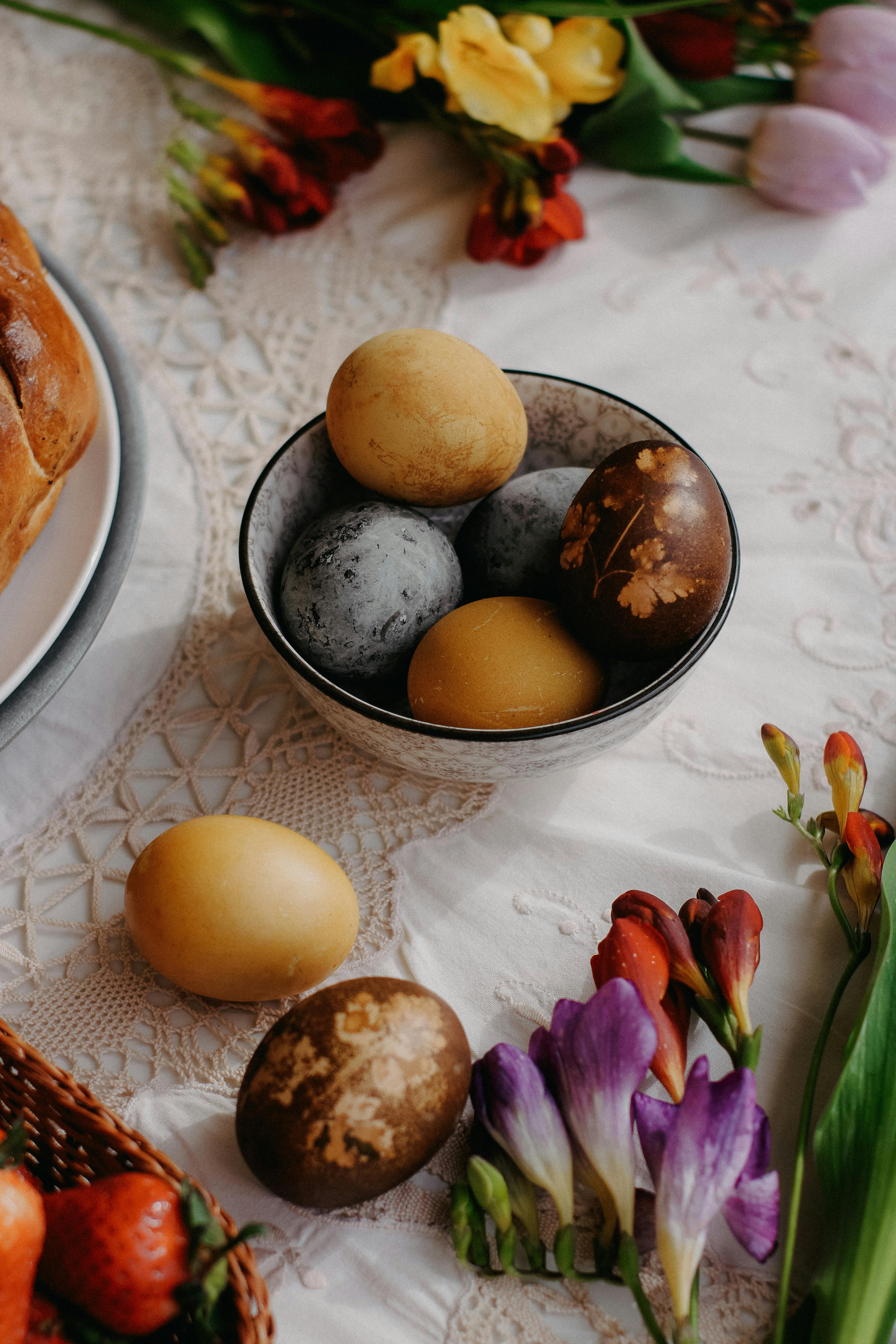 A bowl of painted Easter eggs surrounded by vibrant spring flowers on a dining table, capturing the festive Easter ambiance.