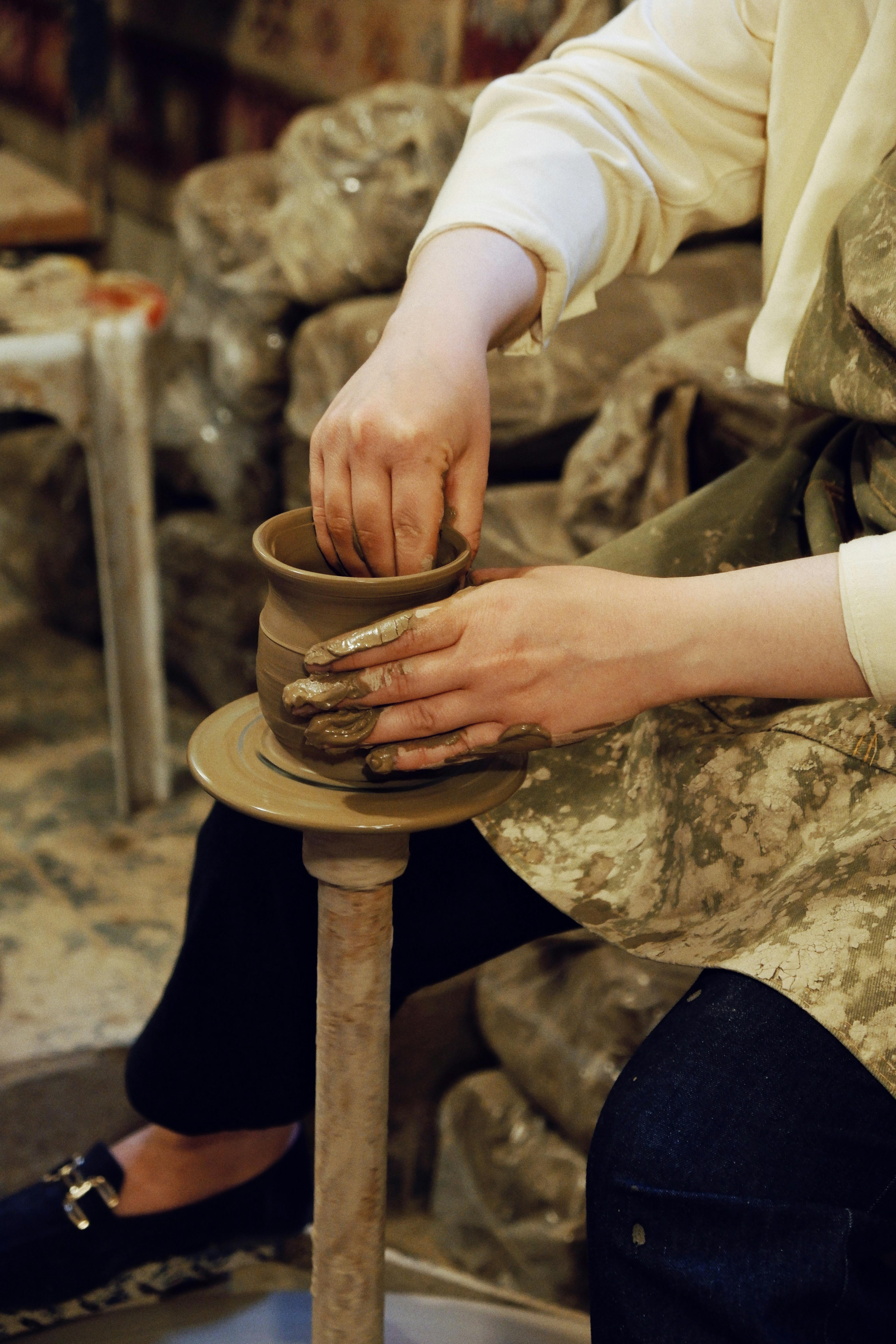 Potter's hands molding clay into shape on a spinning wheel in a workshop setting.