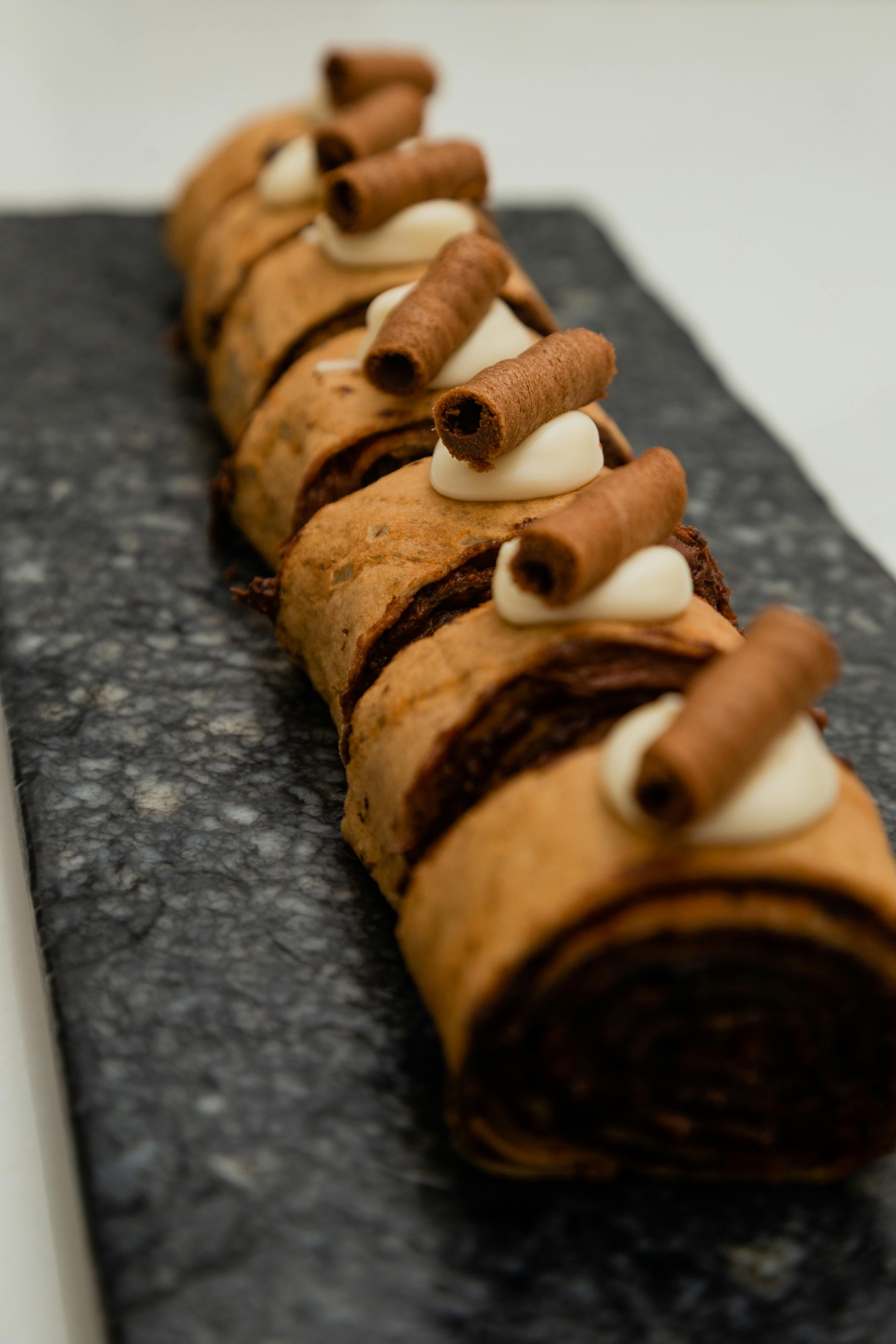 Tempting chocolate Swiss roll topped with cream and cocoa curls on a textured marble slab.