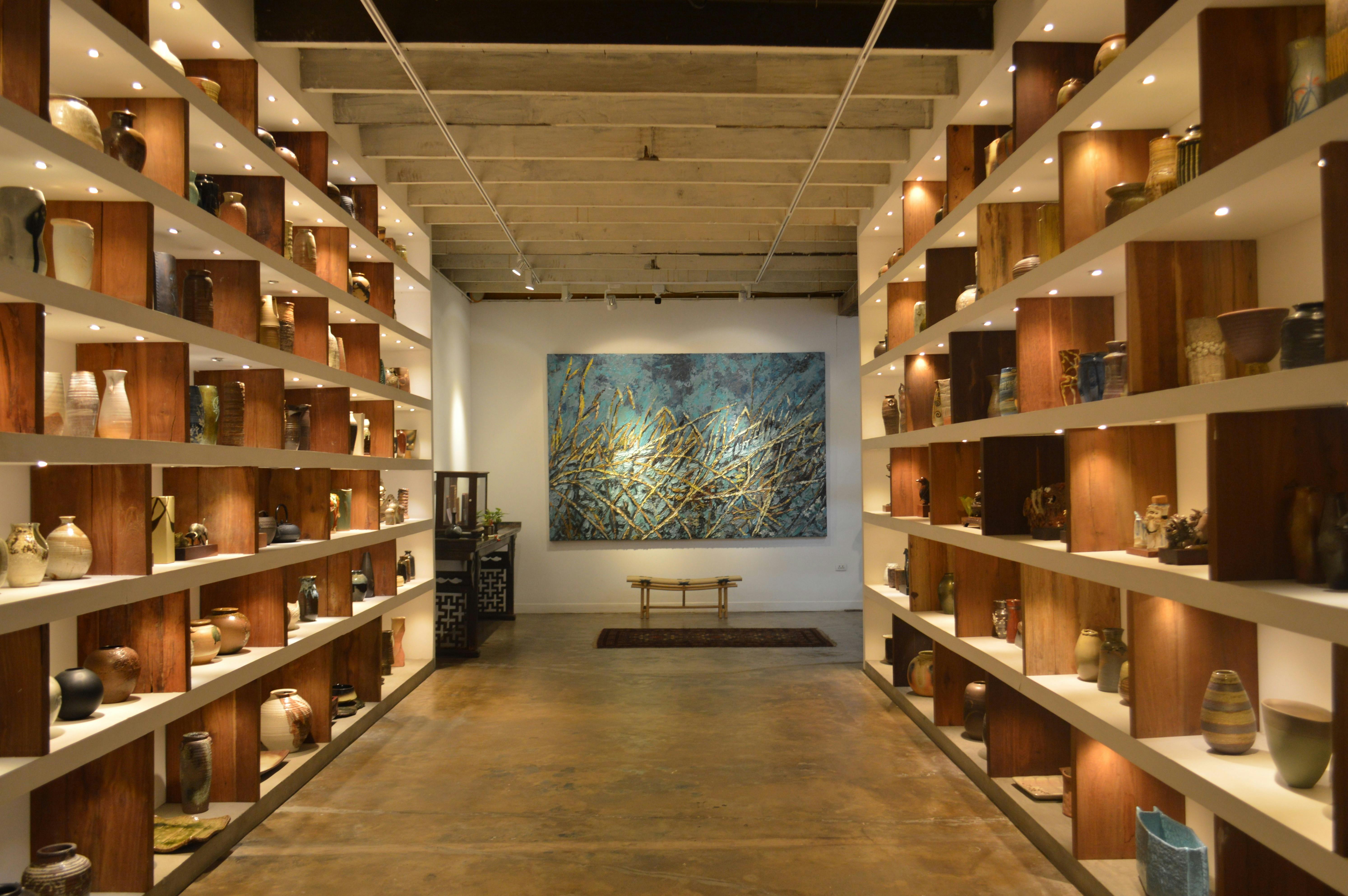 A modern art gallery featuring pottery on shelves and a large abstract painting at the center.