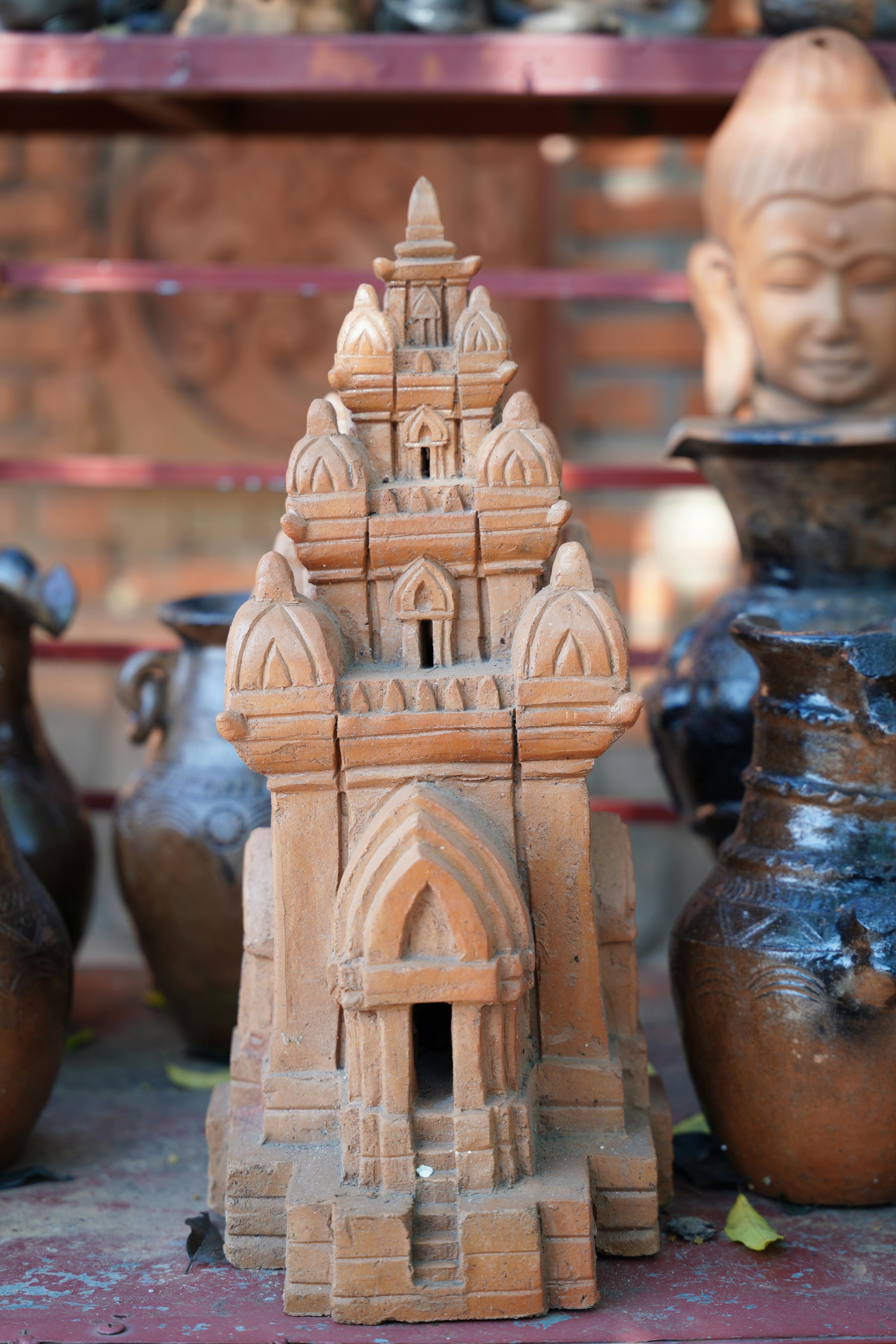 Detailed terracotta miniature temple sculpture surrounded by pottery with a serene atmosphere.