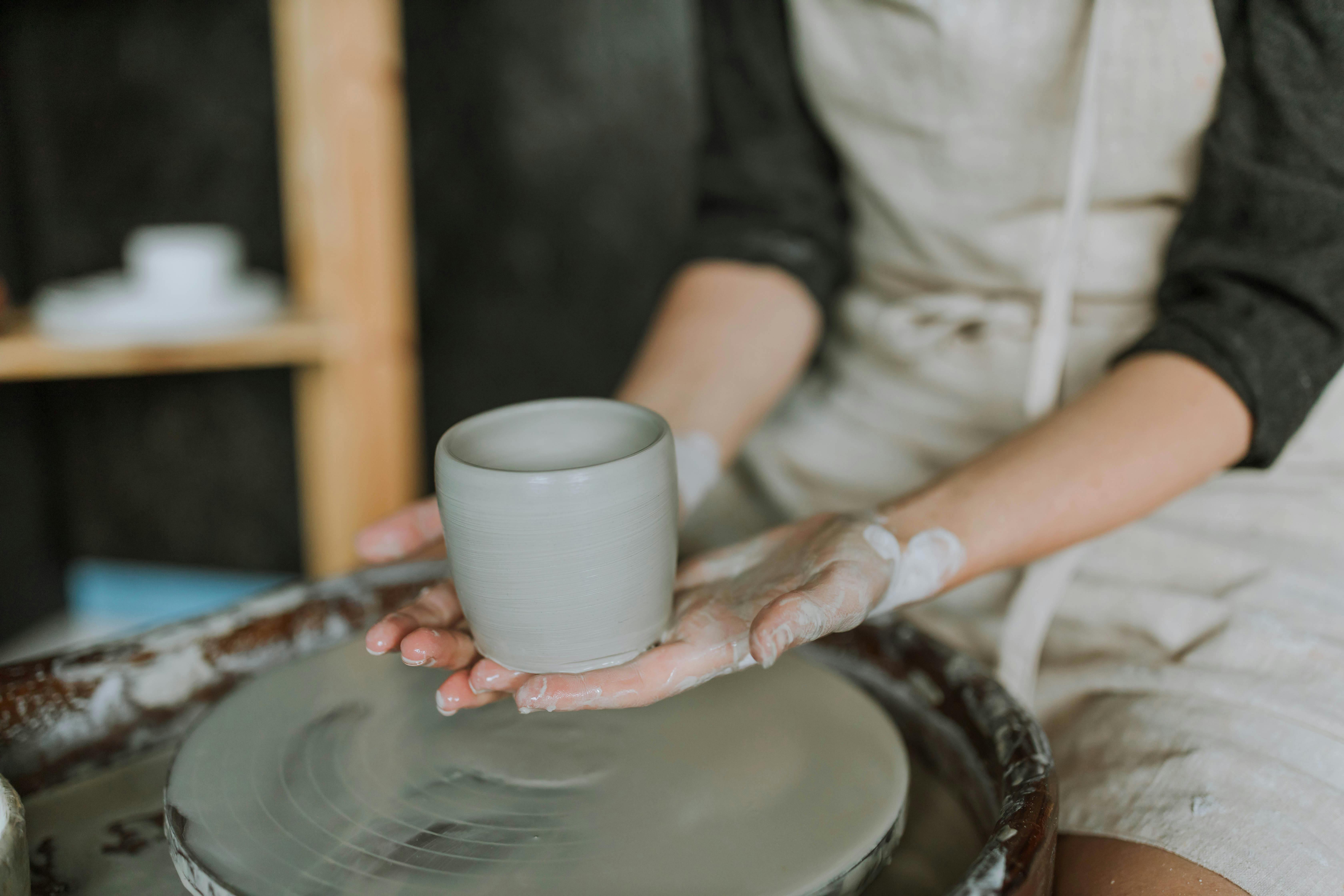 Close-up of craftswoman shaping a clay mug on a pottery wheel in a workshop.