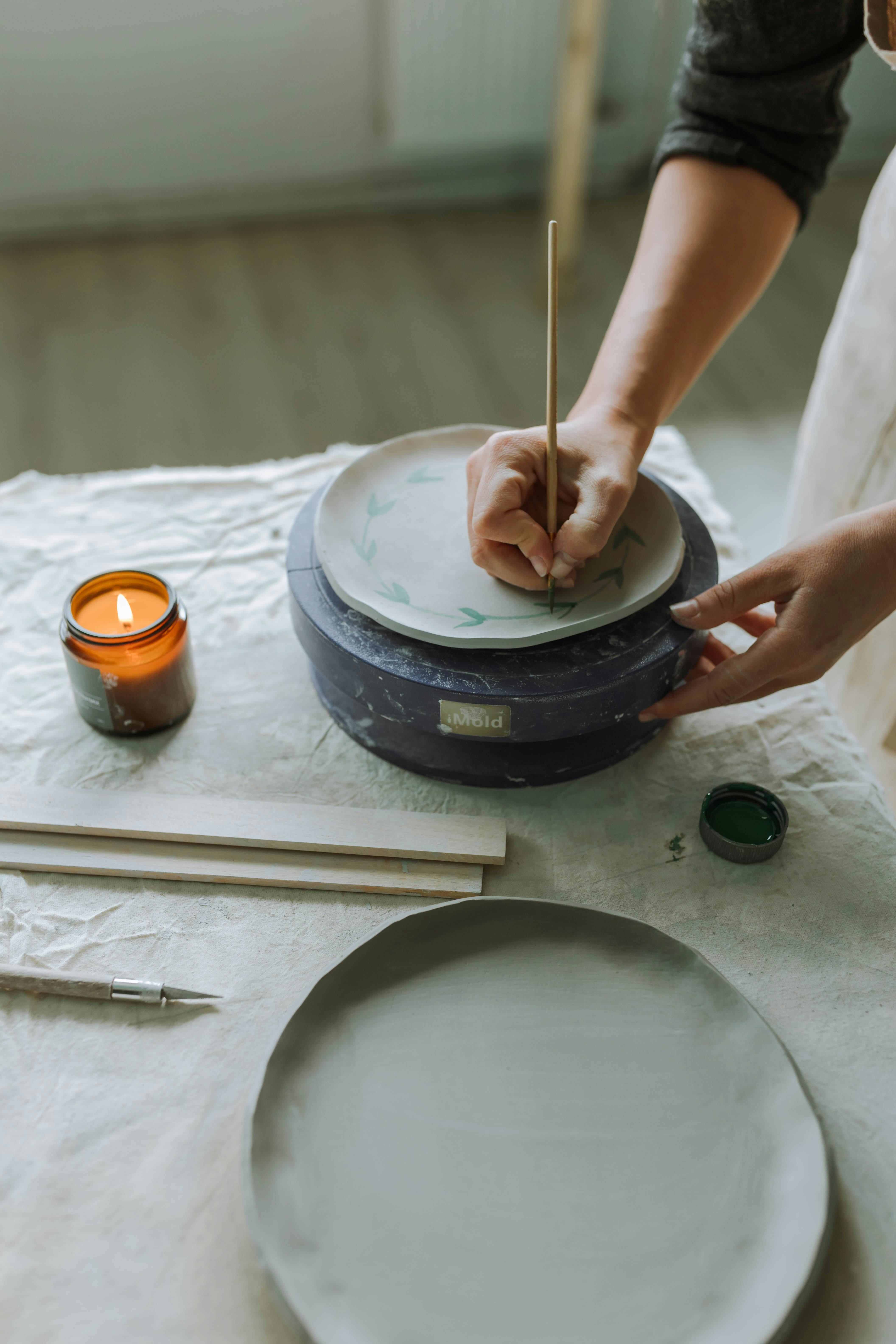 A craftswoman painting a pottery plate with abstract design in a cozy workshop.