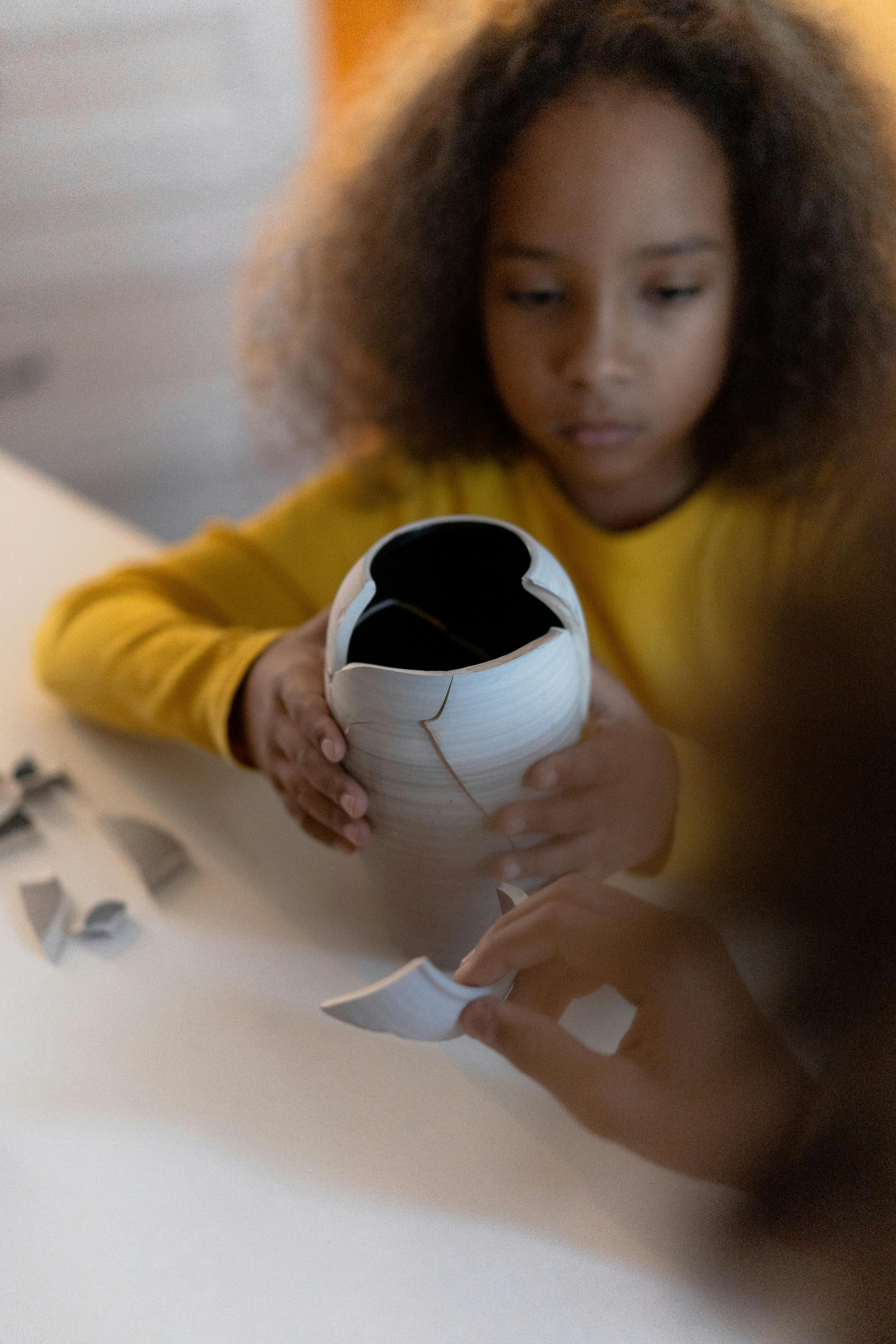 Child with curly hair repairing broken vase, focusing on hands and careful assembly.