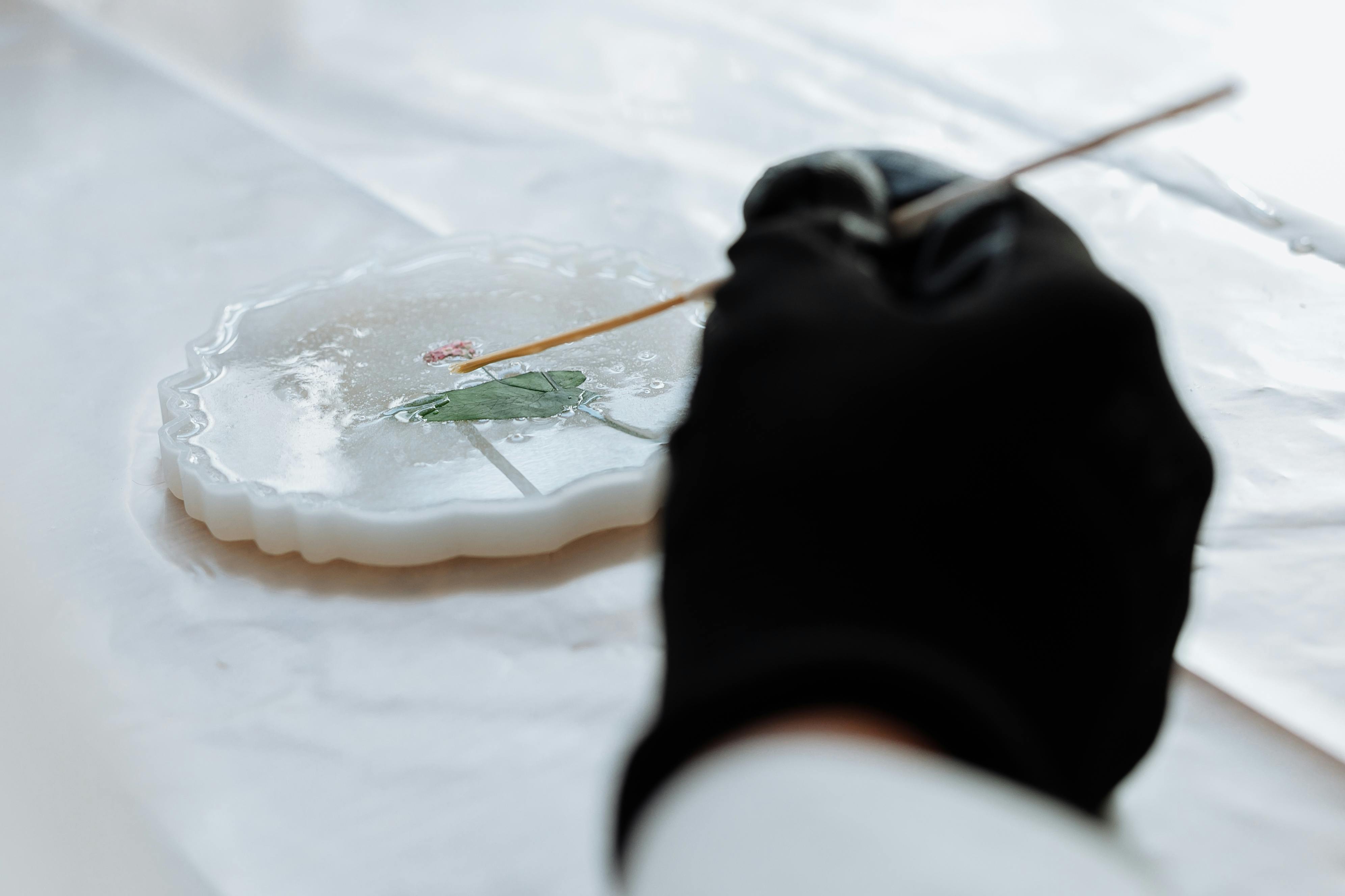 Close-up of hands crafting detailed resin art using a delicate tool, showcasing artistic precision.
