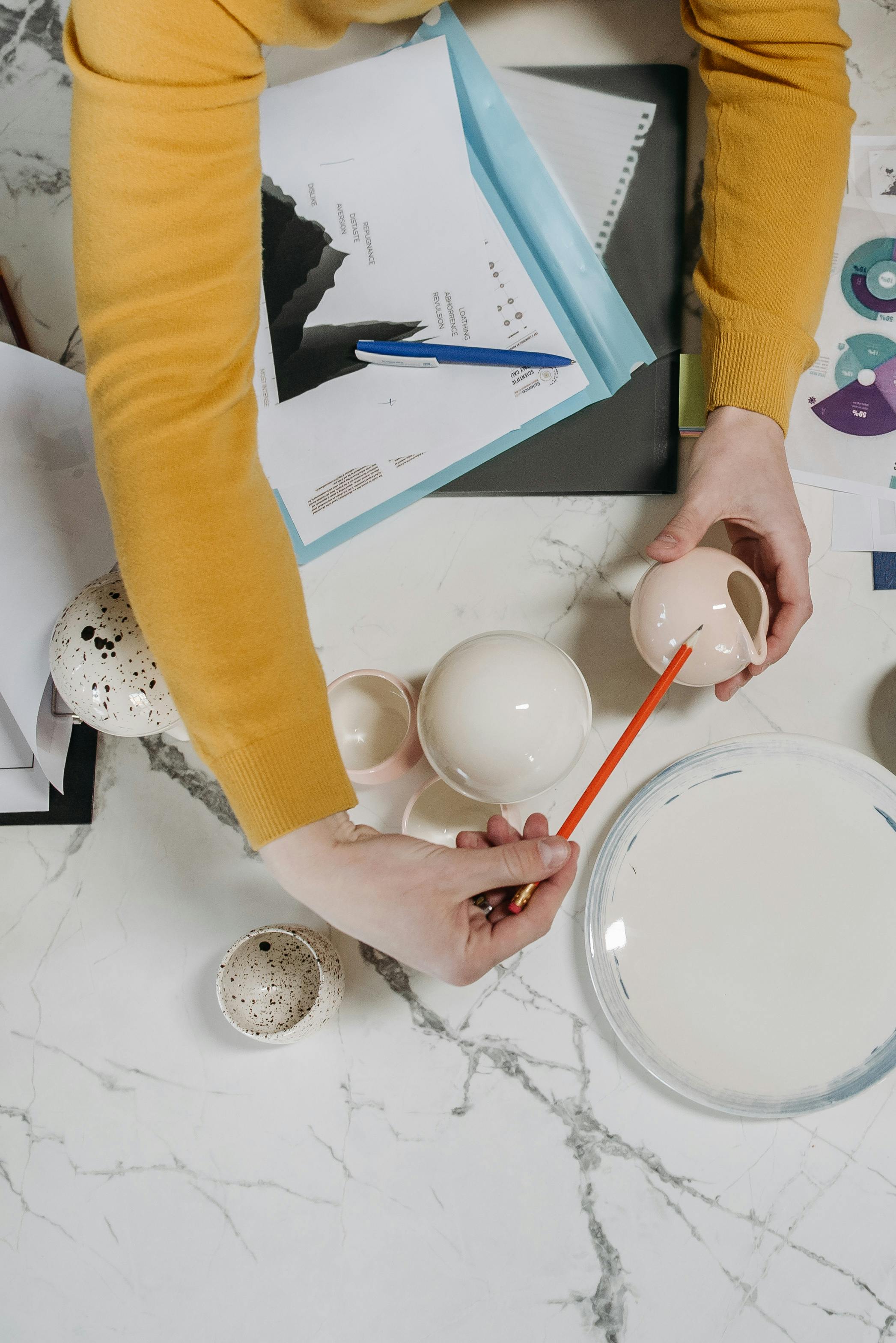 A person skillfully painting handmade ceramic items on a marble table, showcasing craftsmanship.
