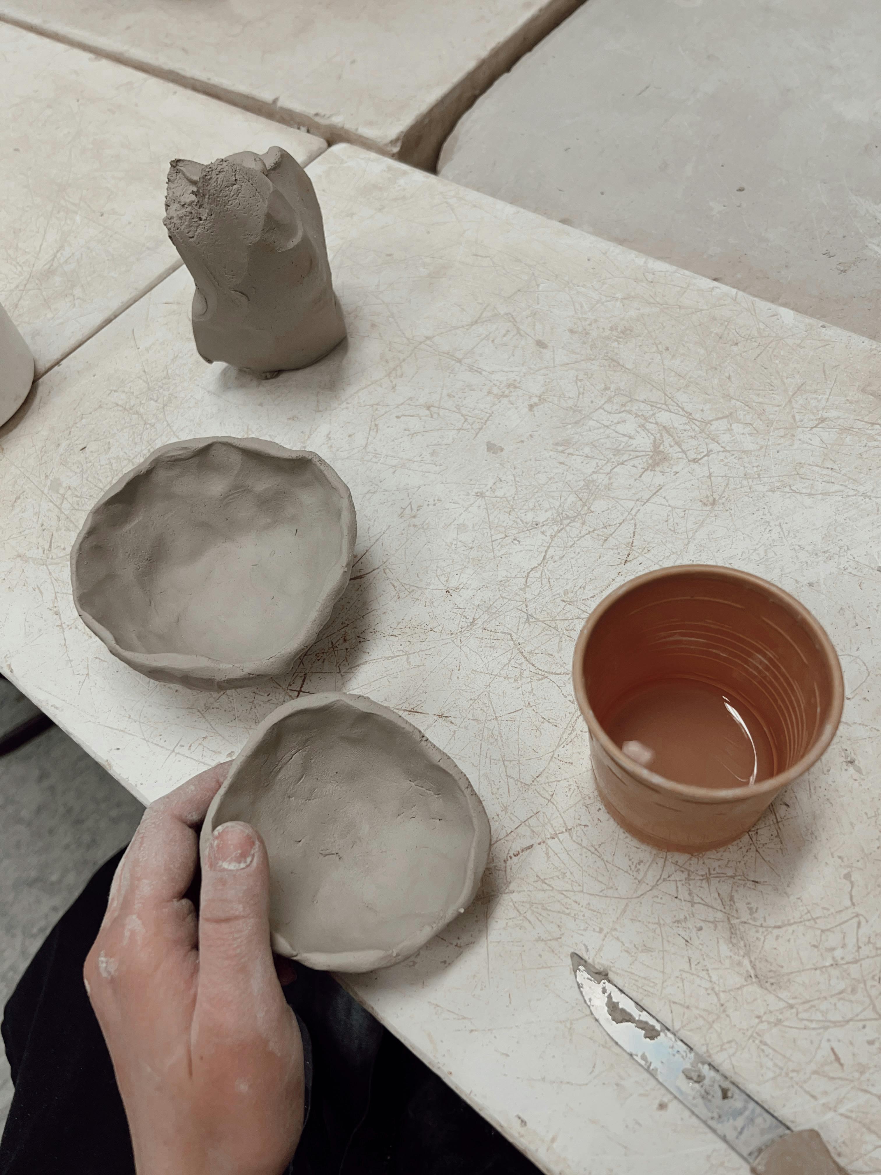 Artisan handcrafting clay bowls and a cup on a pottery table.