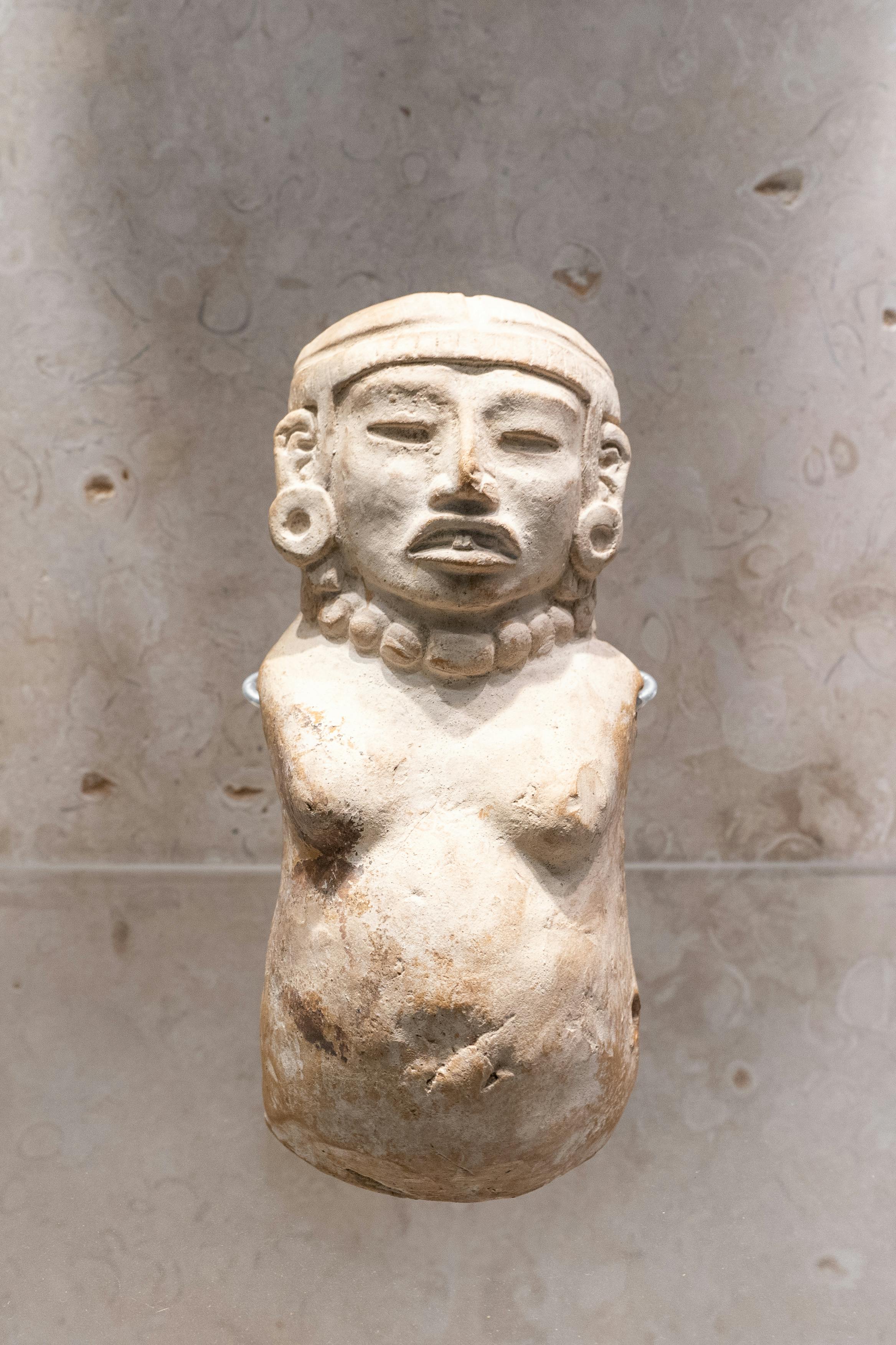 Ancient Mayan figurine statue displayed against textured stone wall.