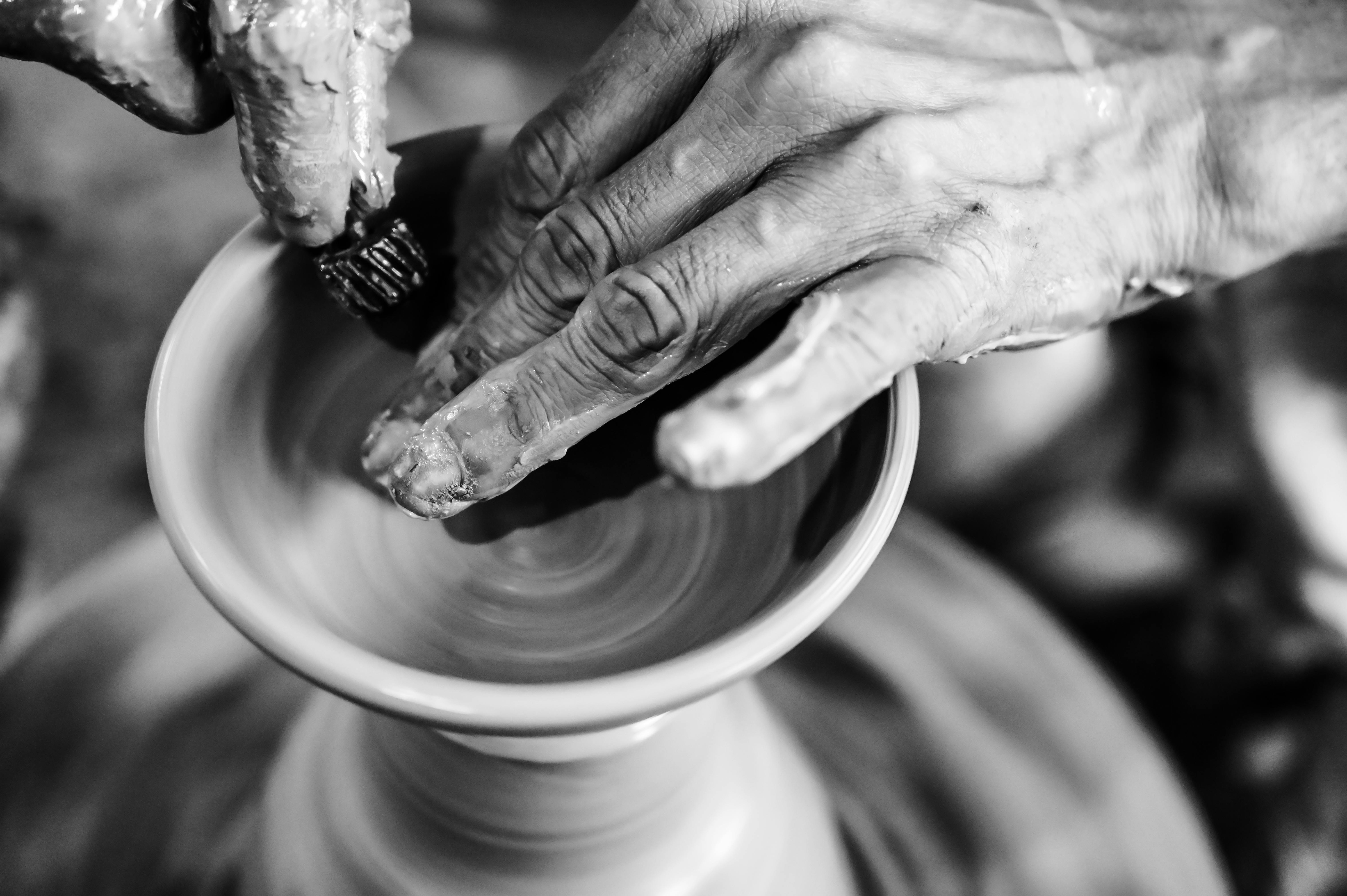 Black and white photo of hands crafting pottery on a wheel, emphasizing texture and detail.