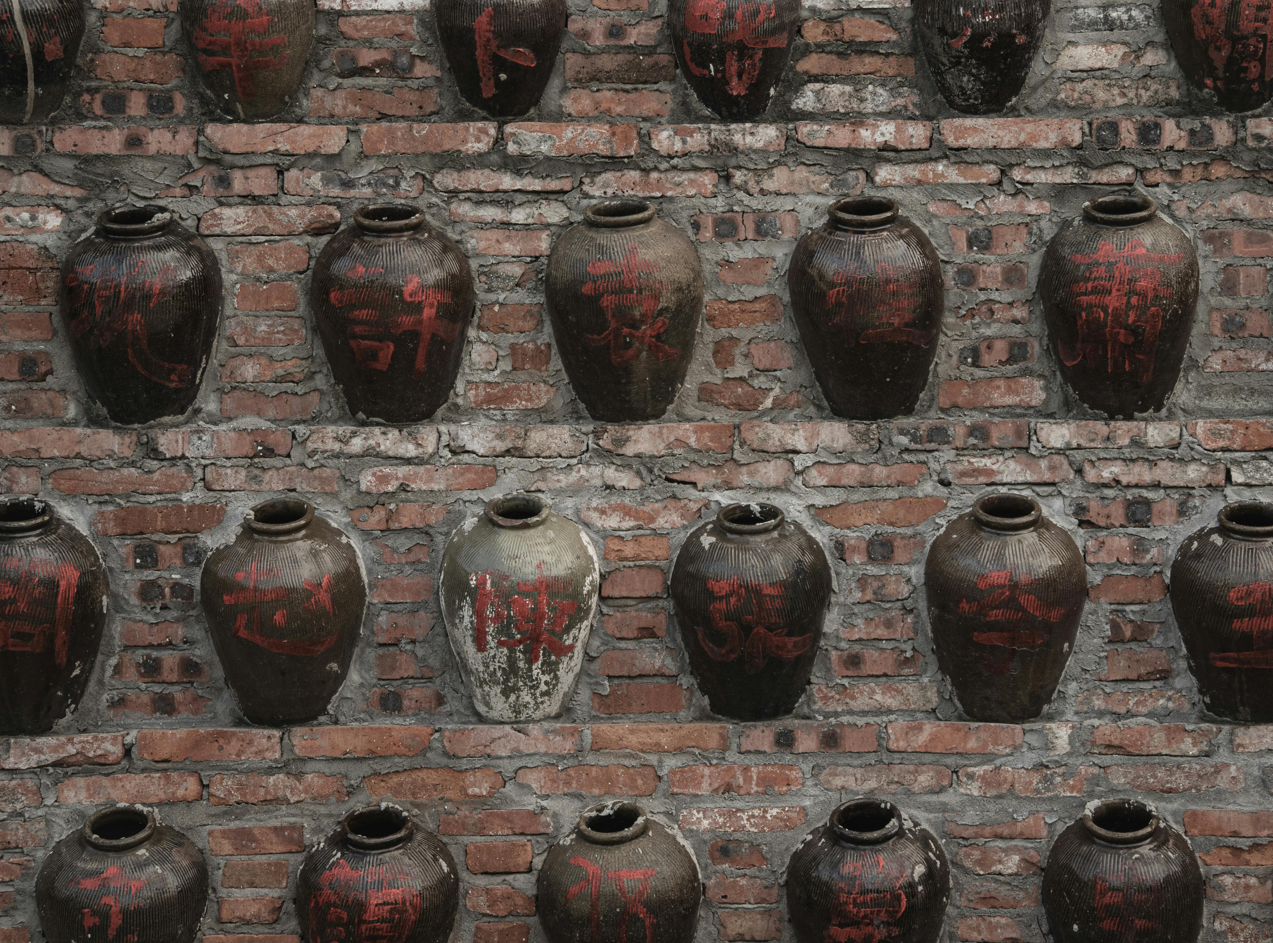Vintage clay jars with Chinese characters on rustic brick wall, creating traditional artistic display.