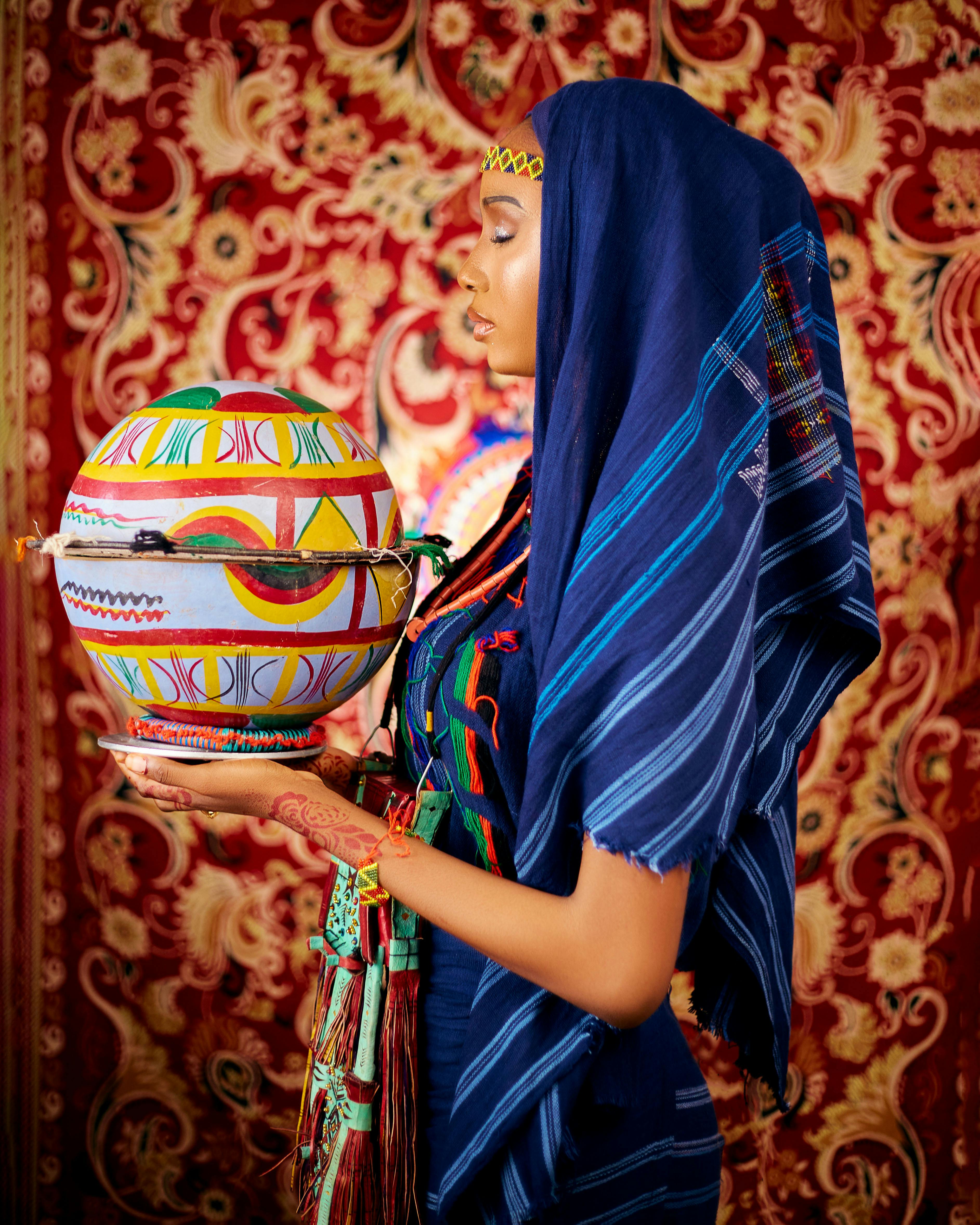 Vibrant portrait of a woman in traditional attire holding colorful pottery against an ornate backdrop.