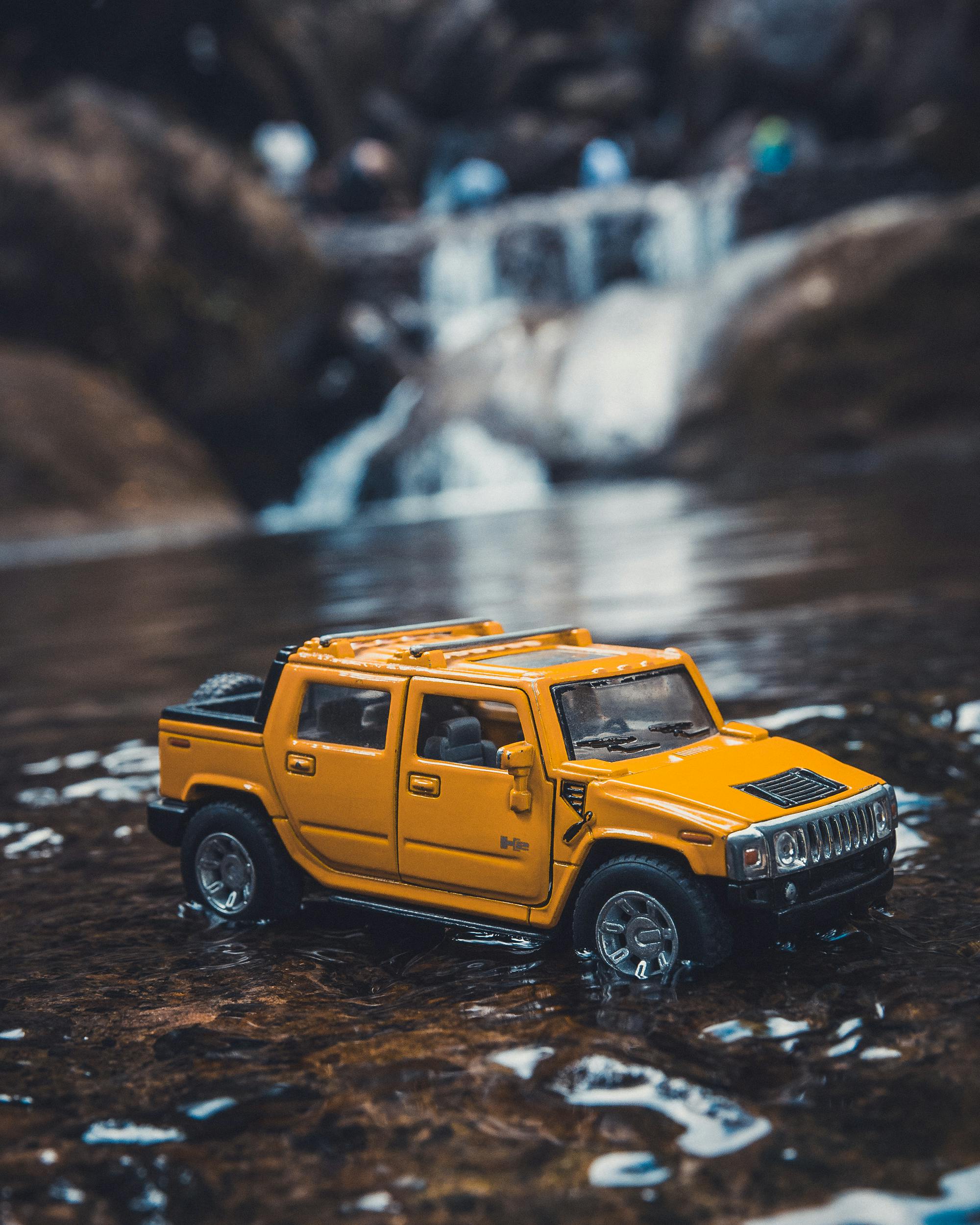 A detailed toy SUV car parked on a wet surface near a small waterfall in Cherrapunji, India.
