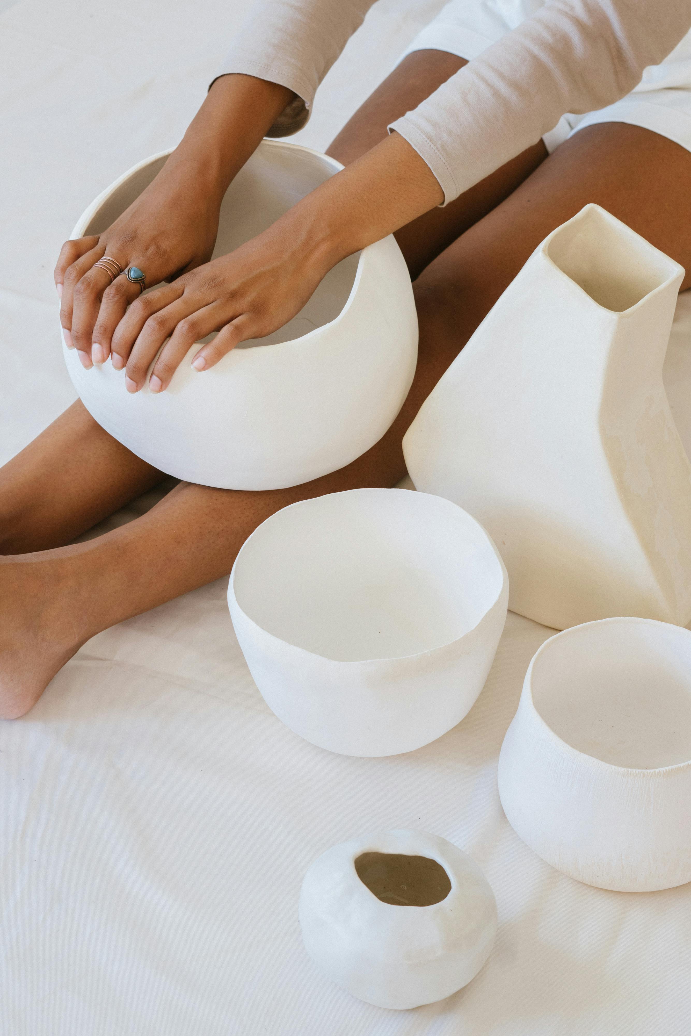 Top view of a woman crafting white ceramic pottery pieces, showcasing artisan skills and minimalist design.