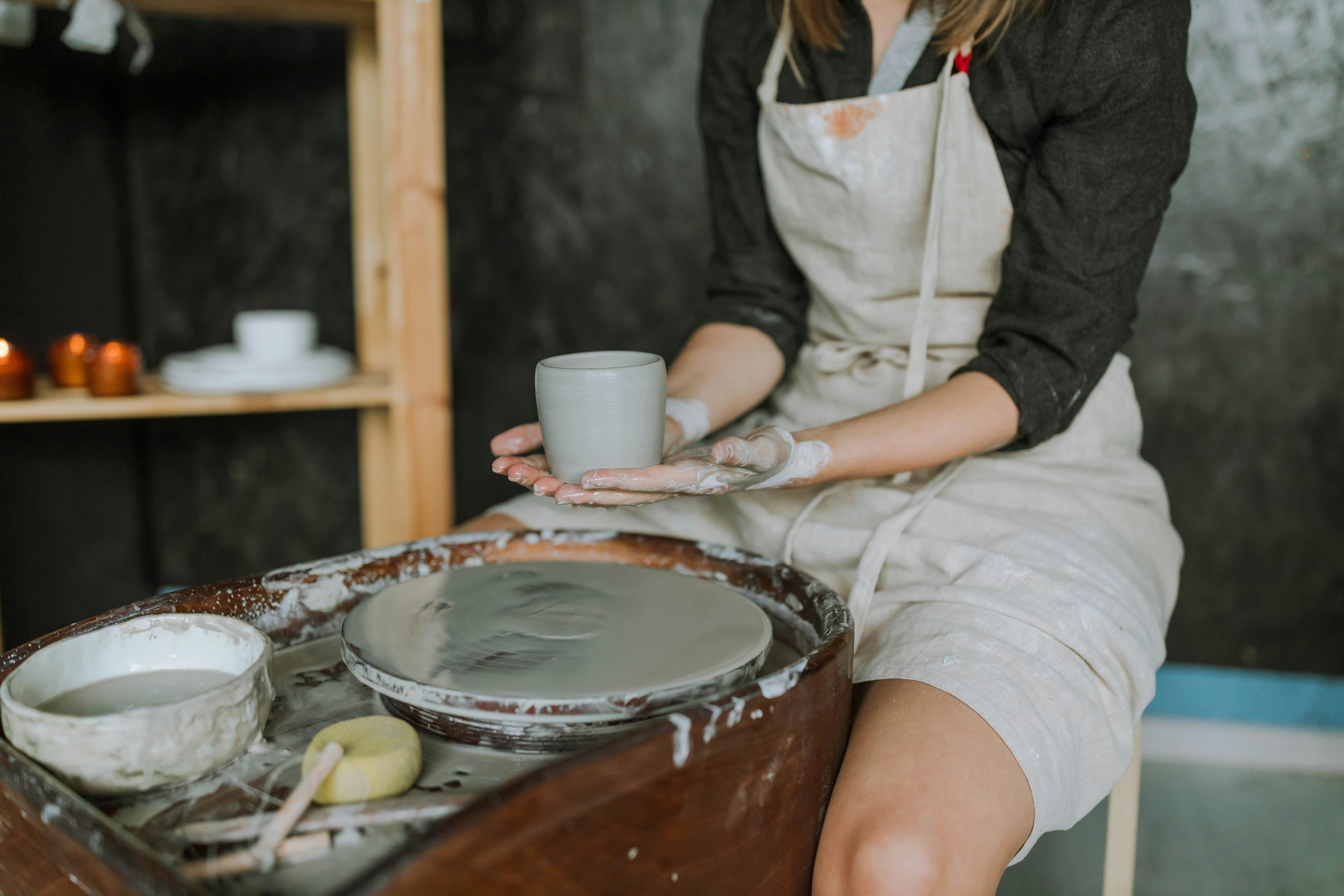 Craftswoman shaping ceramic pottery on wheel in indoor workshop.