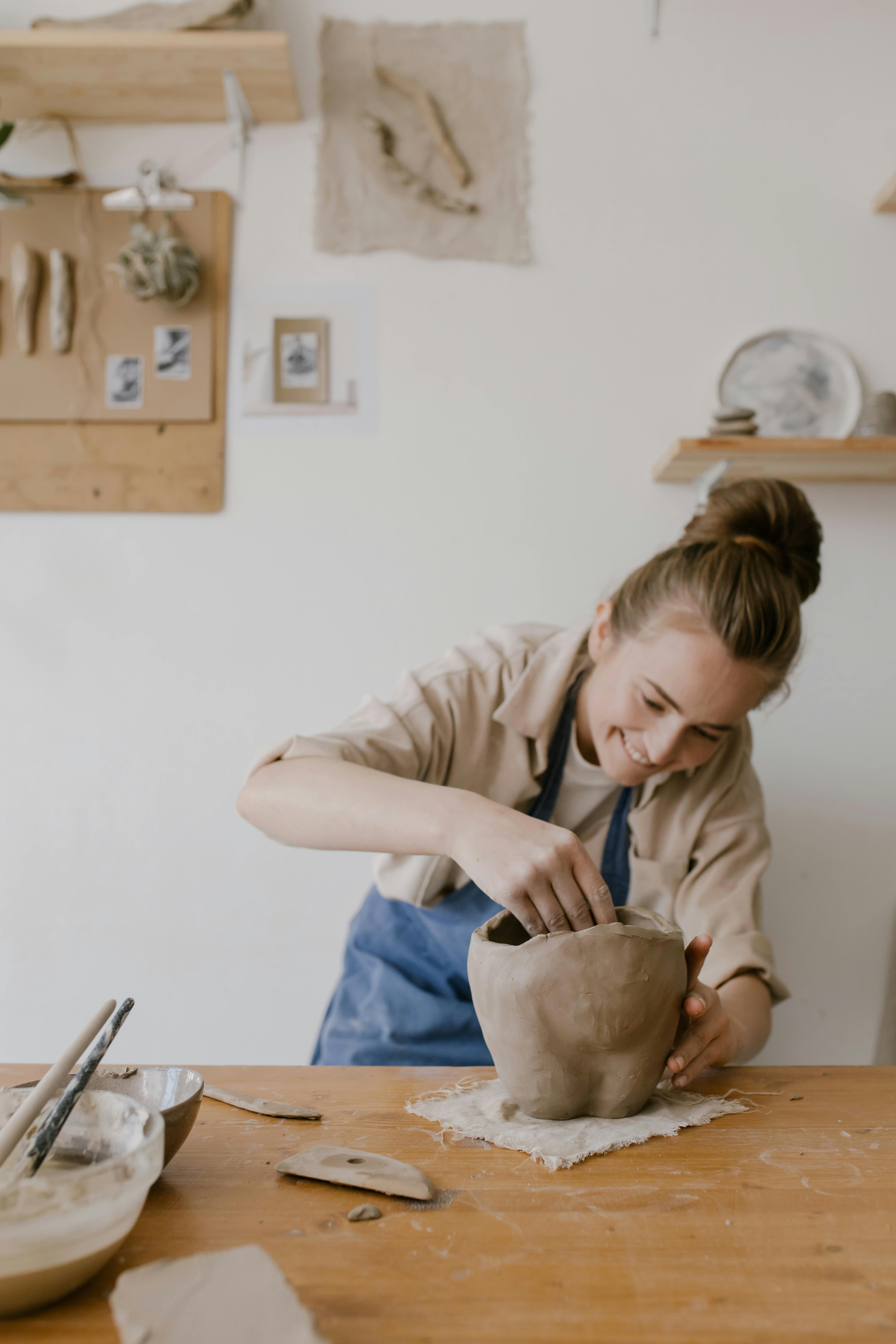 A woman shaping pottery clay in her arts and crafts workshop, showcasing her skill and passion.