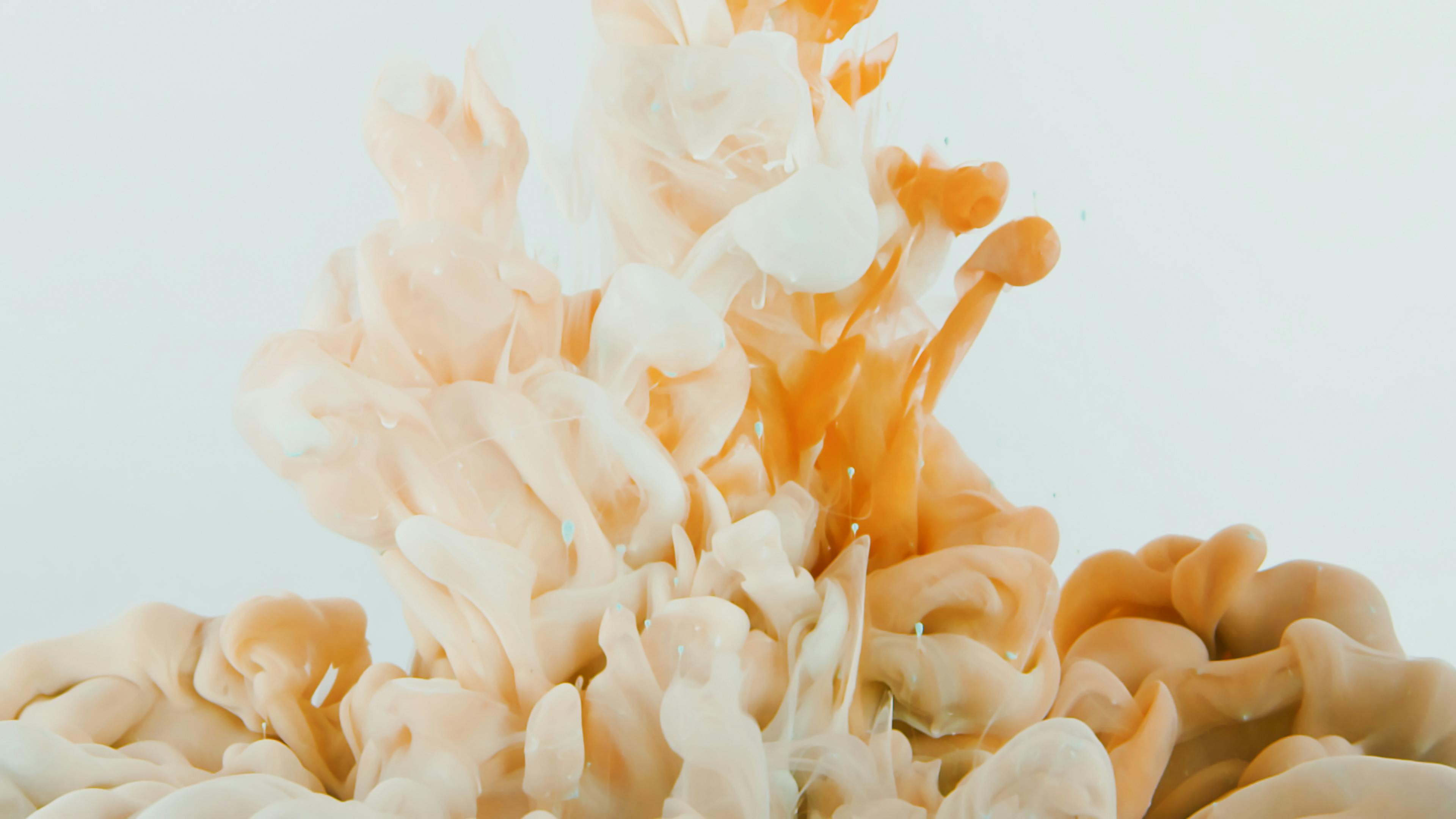 Close-up of swirling orange and white liquid creating dynamic abstract patterns on a white background.