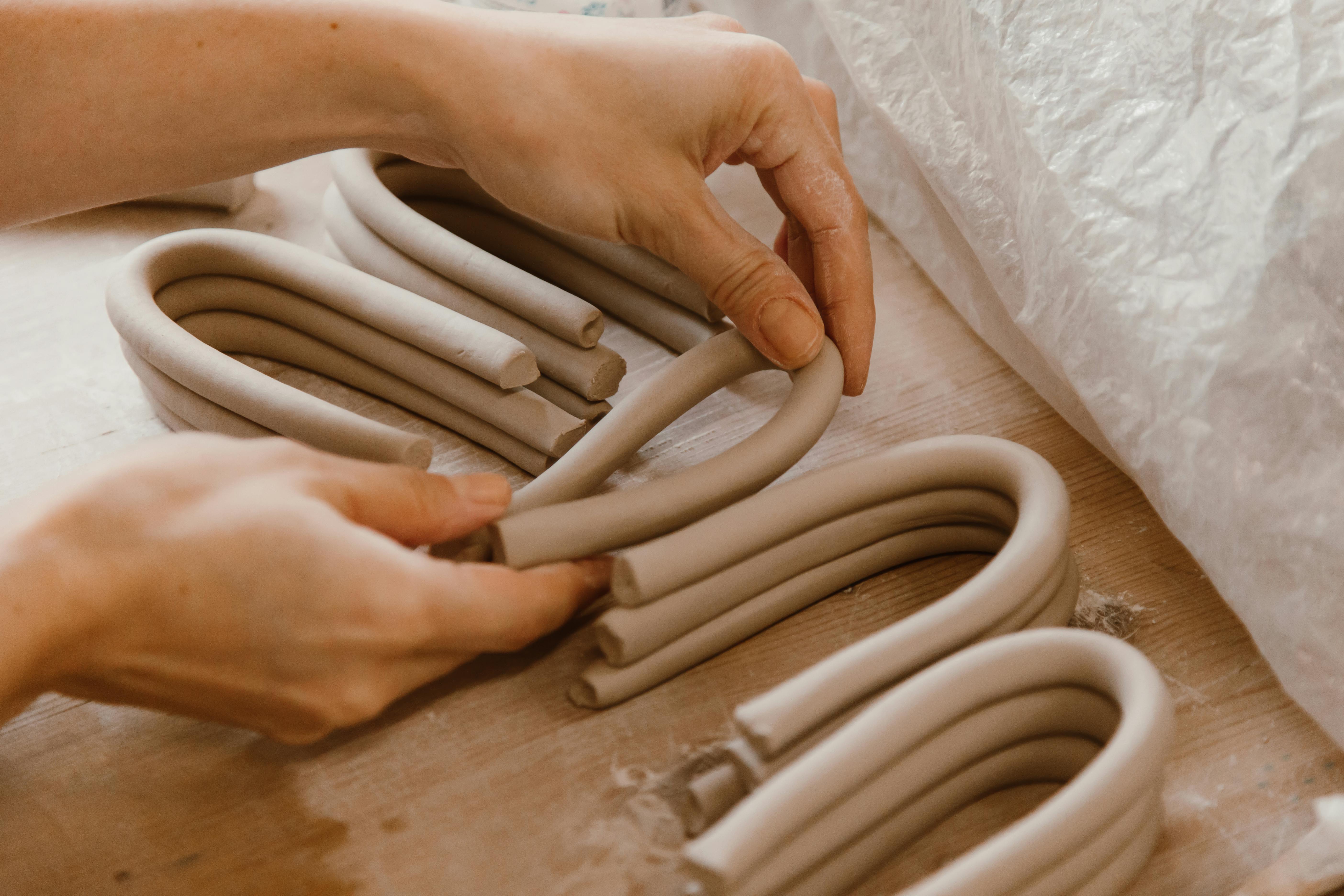 Close-up of hands shaping clay coils for pottery, showcasing artisan craftsmanship indoors.
