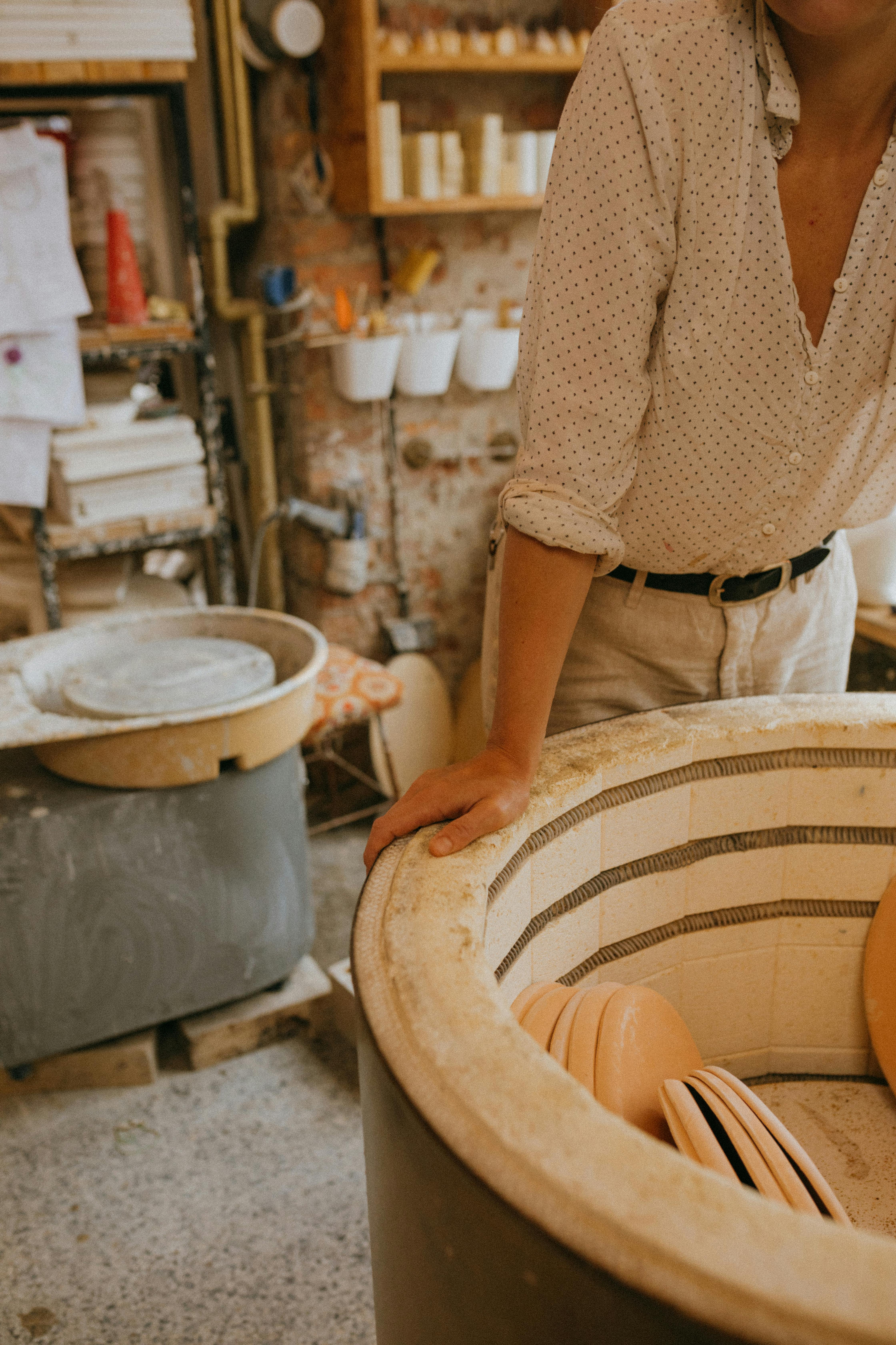 A dedicated artisan working in a pottery workshop with a kiln and various ceramic pieces on display.