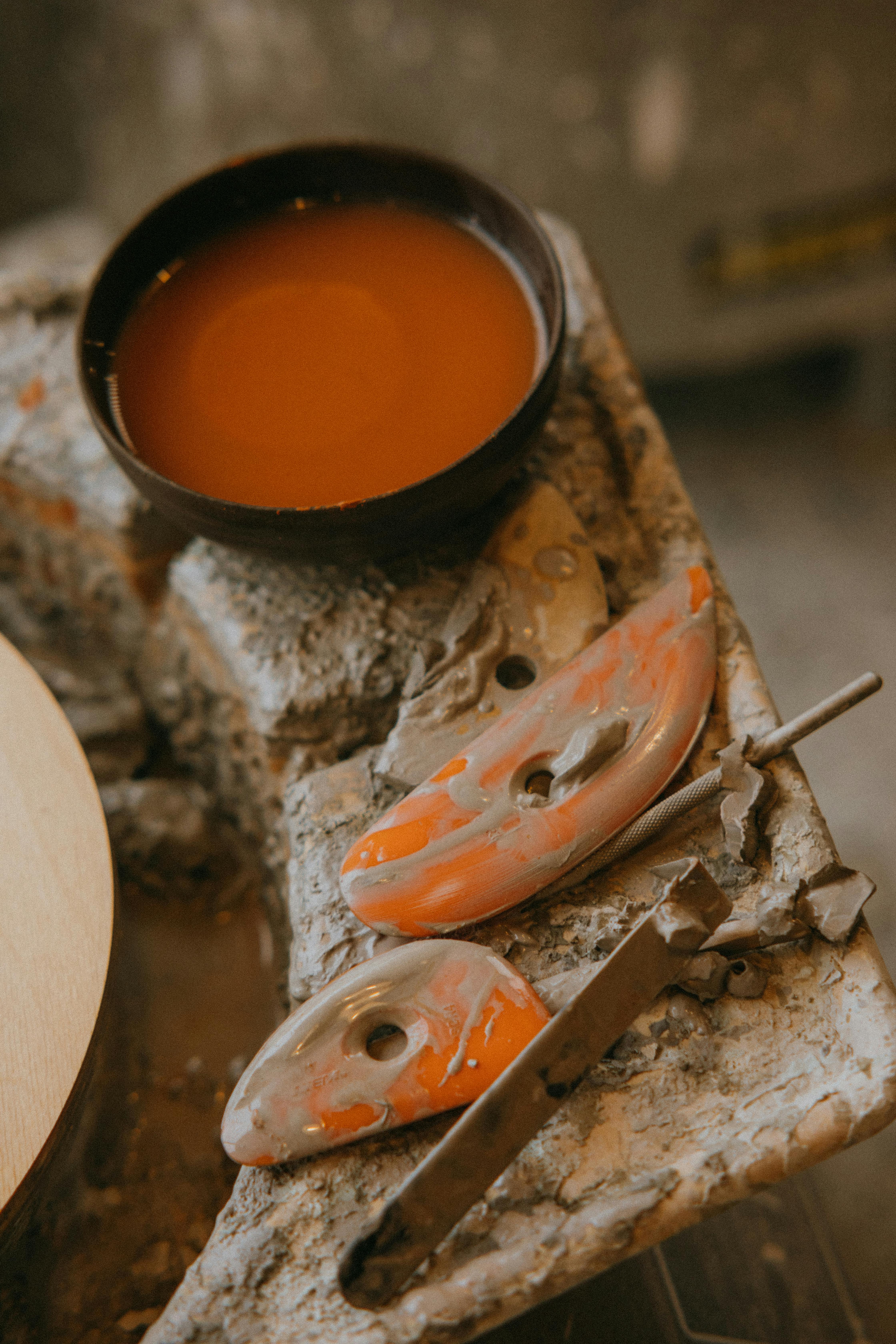 Close-up of pottery tools and glaze on a ceramic workshop table.