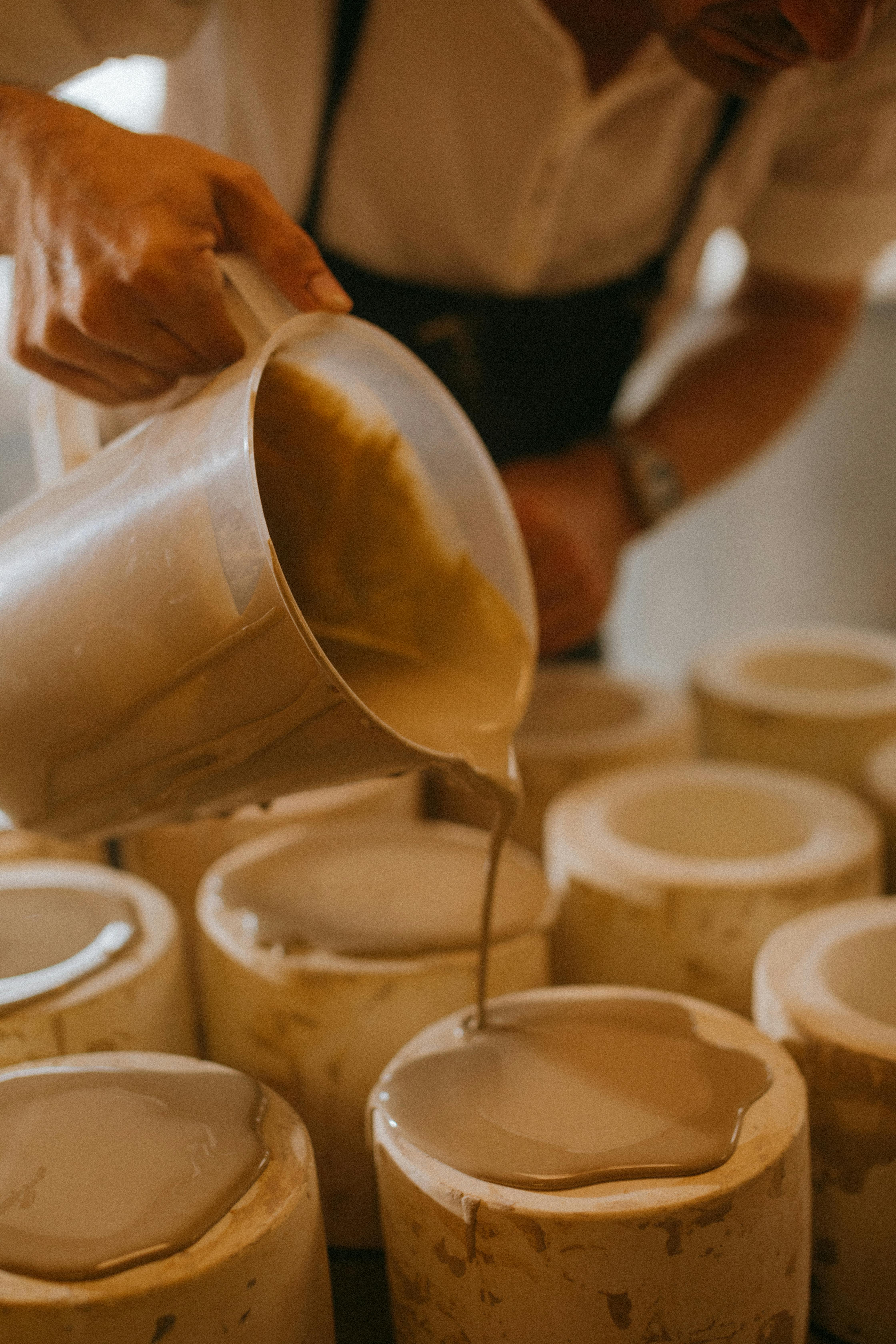 A craftsman skillfully pours ceramic mixture into molds in a workshop setting.