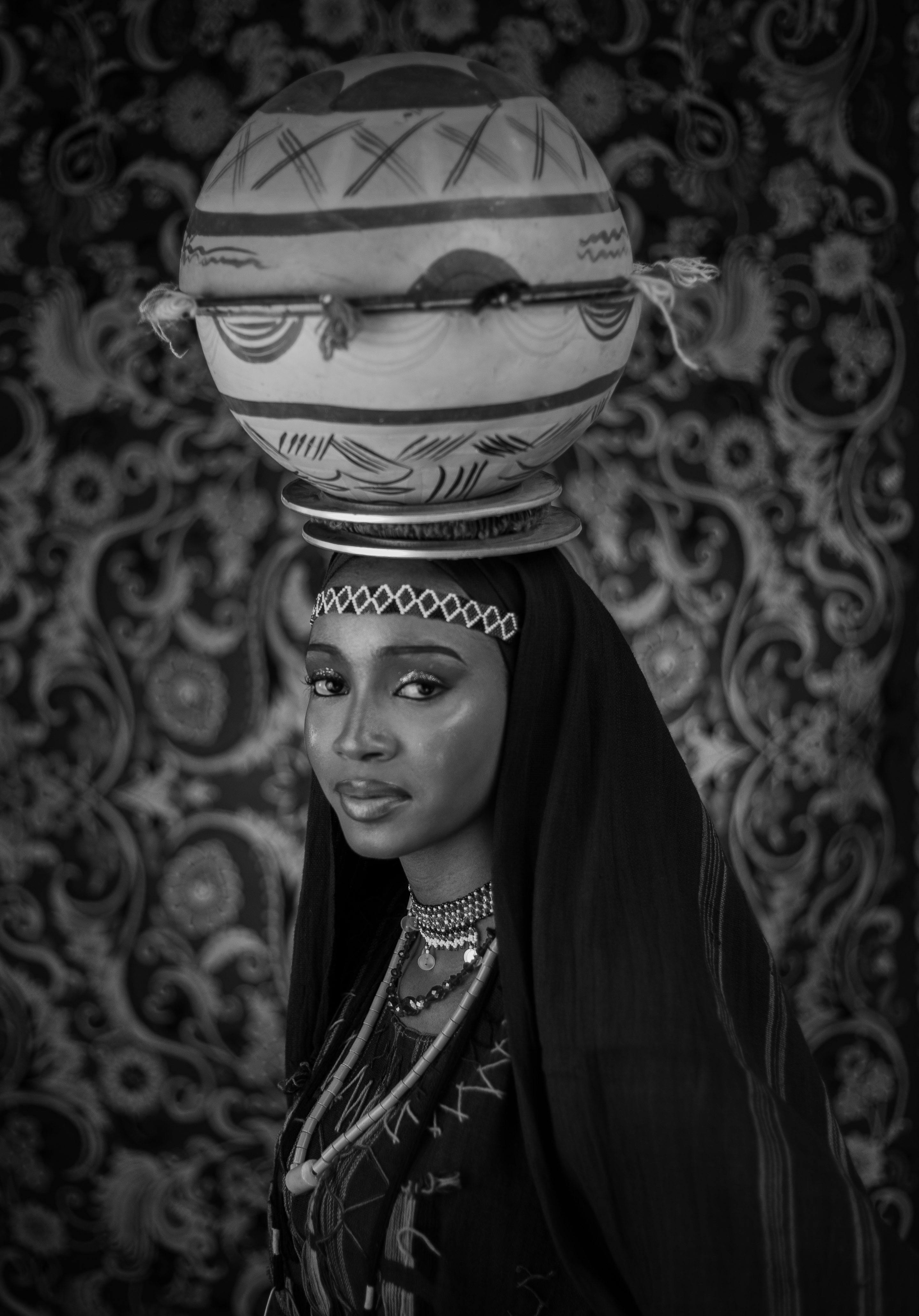 Black and white portrait of a woman in traditional attire with decorative pottery.