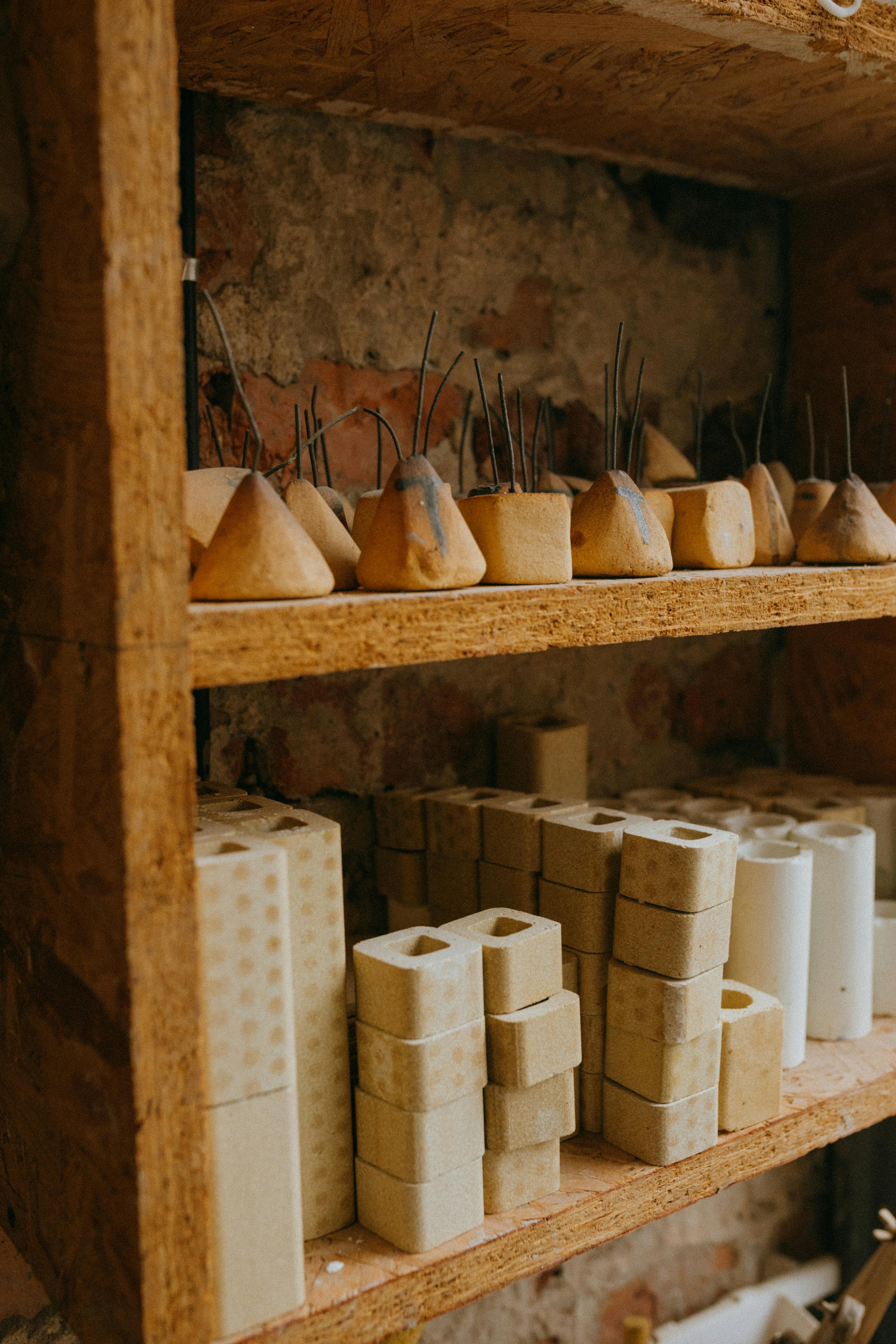 Collection of rustic ceramic molds on wooden shelves in a pottery workshop.