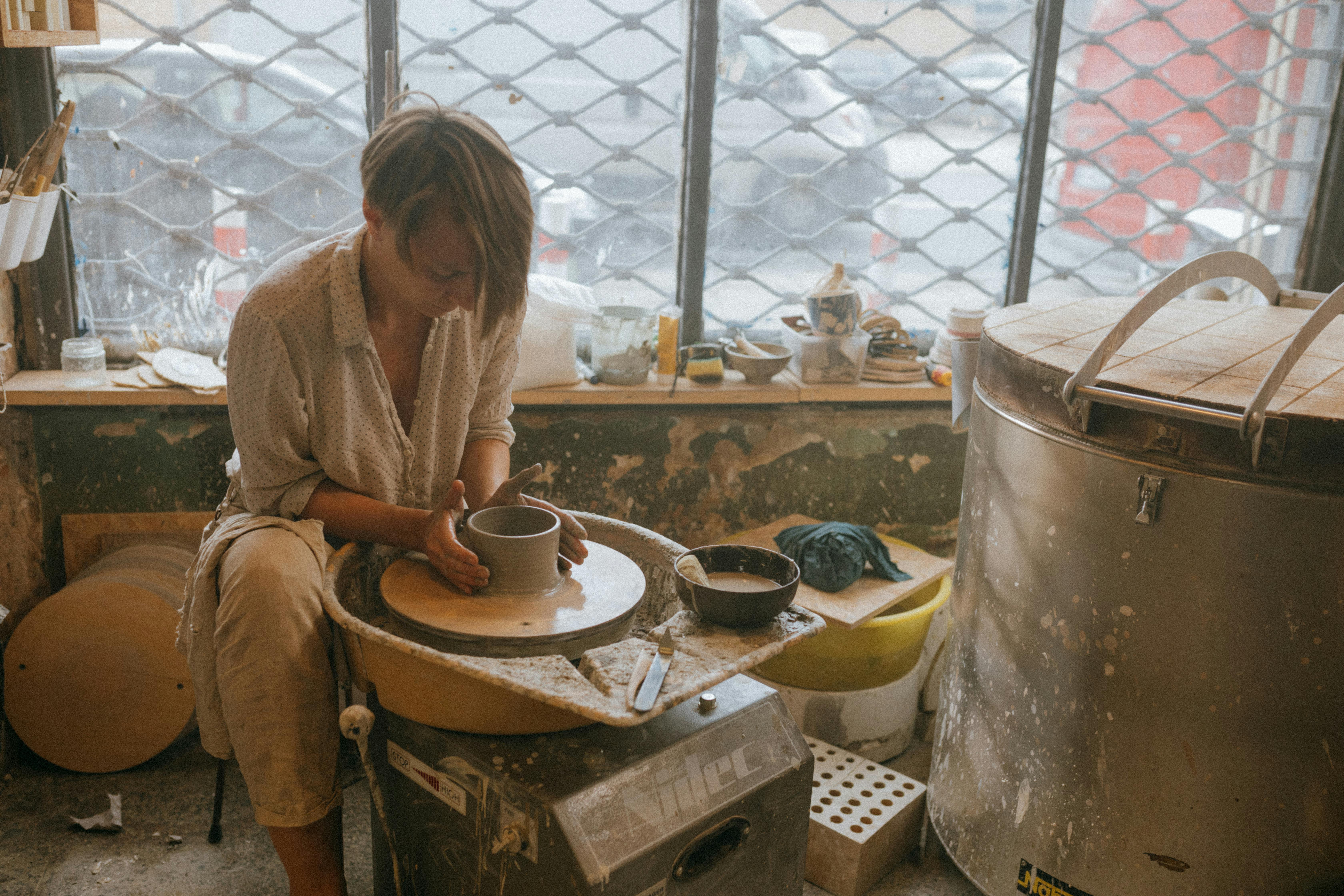 A focused artisan skillfully shapes clay on a pottery wheel in a rustic workshop setting.